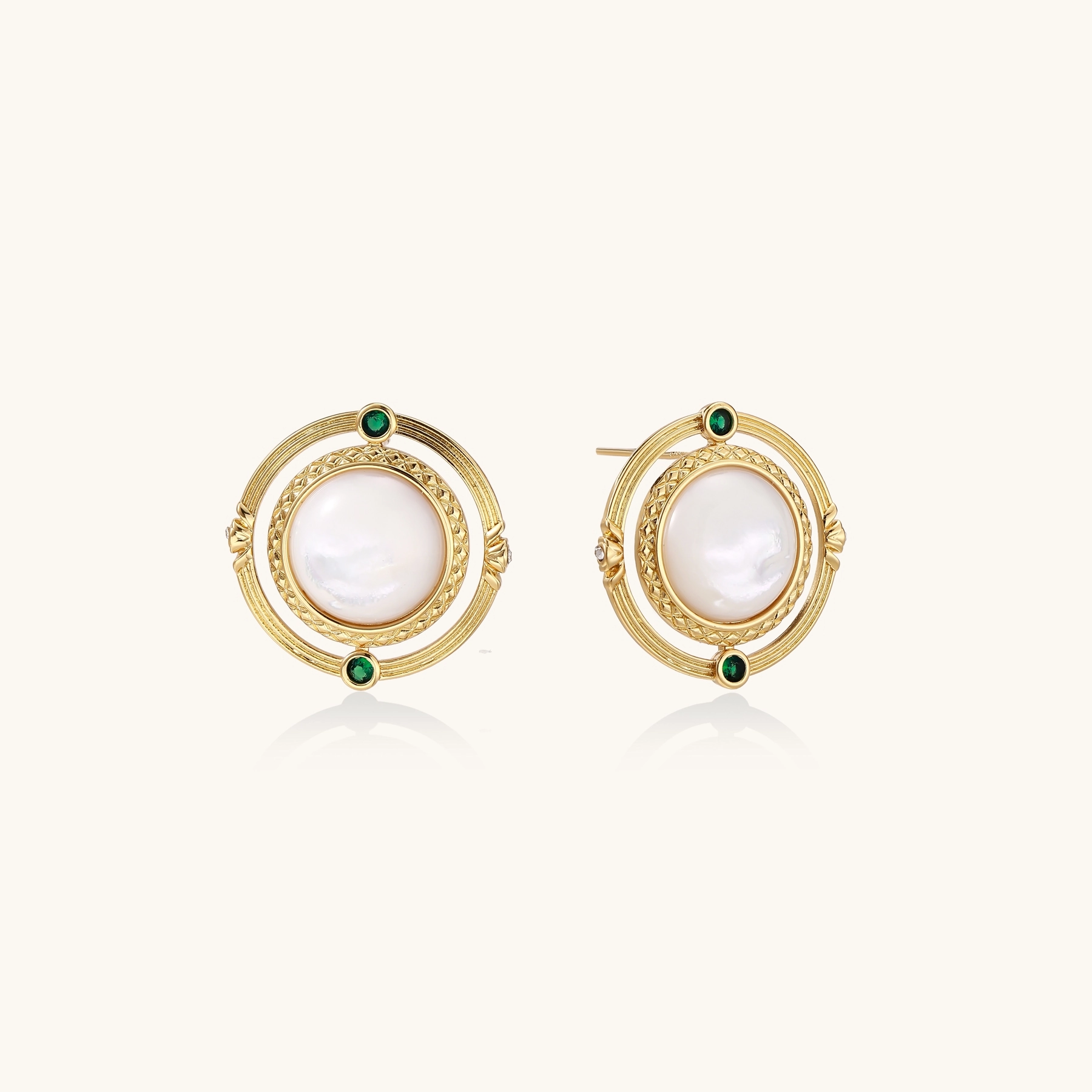 Circular gold stud earrings with iridescent mother-of-pearl center and green zirconia accents on cream background.