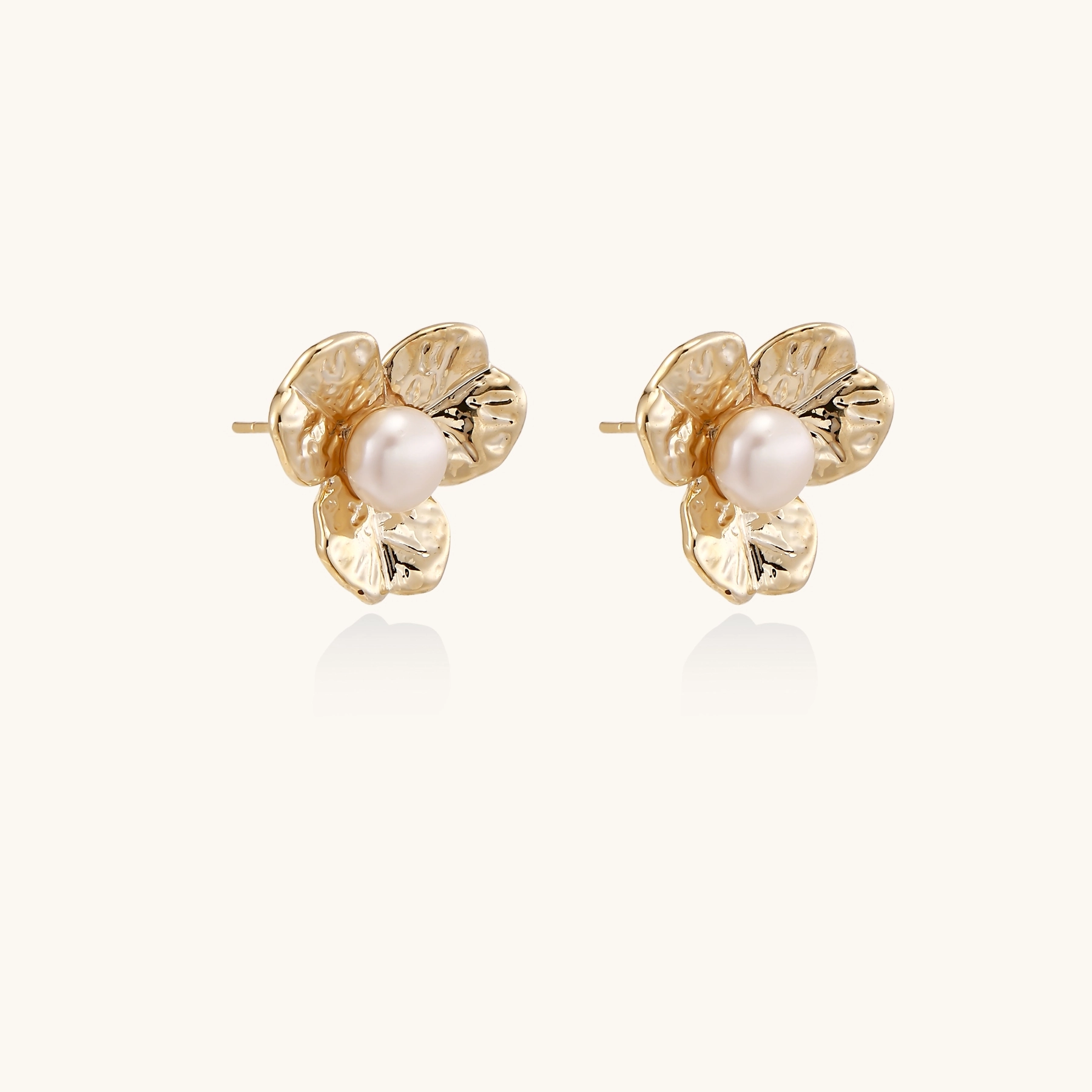 Gold-plated flower stud earrings with textured petals and centered freshwater pearl on beige background