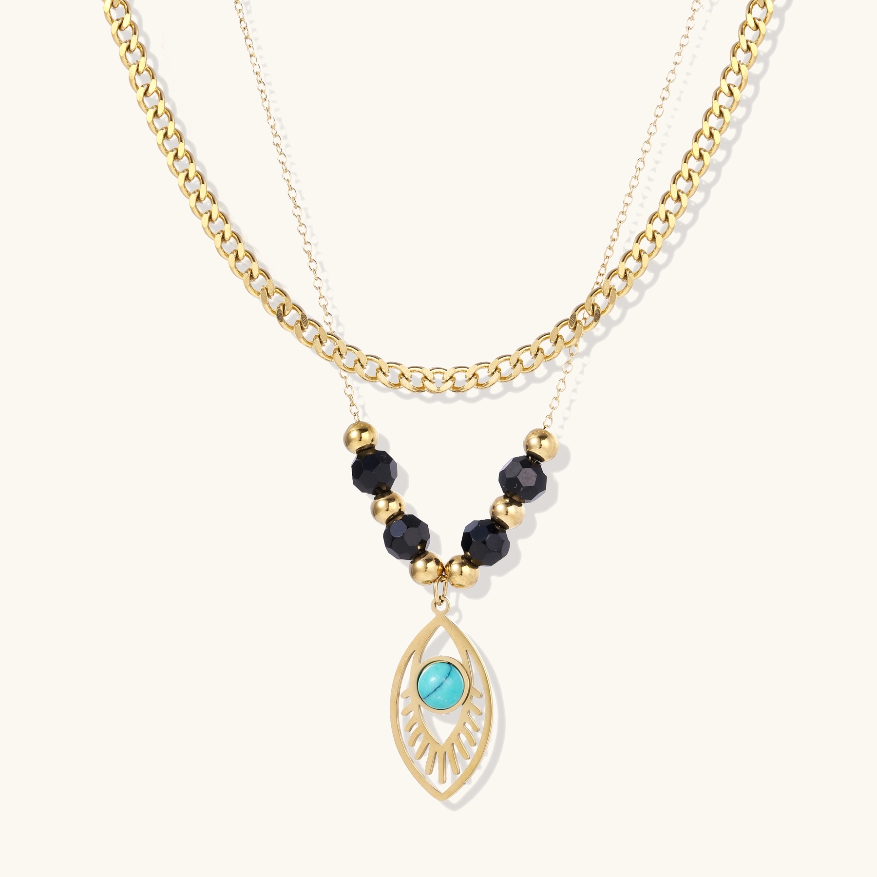 Layered gold necklace with turquoise evil eye pendant and black quartz beads on cream background