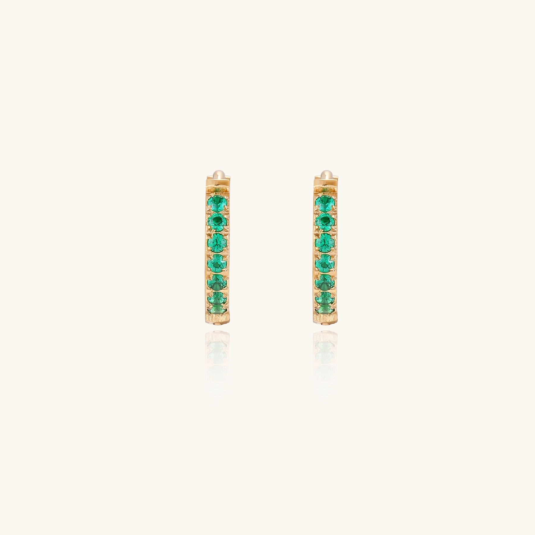 Pair of small gold huggie hoop earrings with bright green cubic zirconia stones on cream background