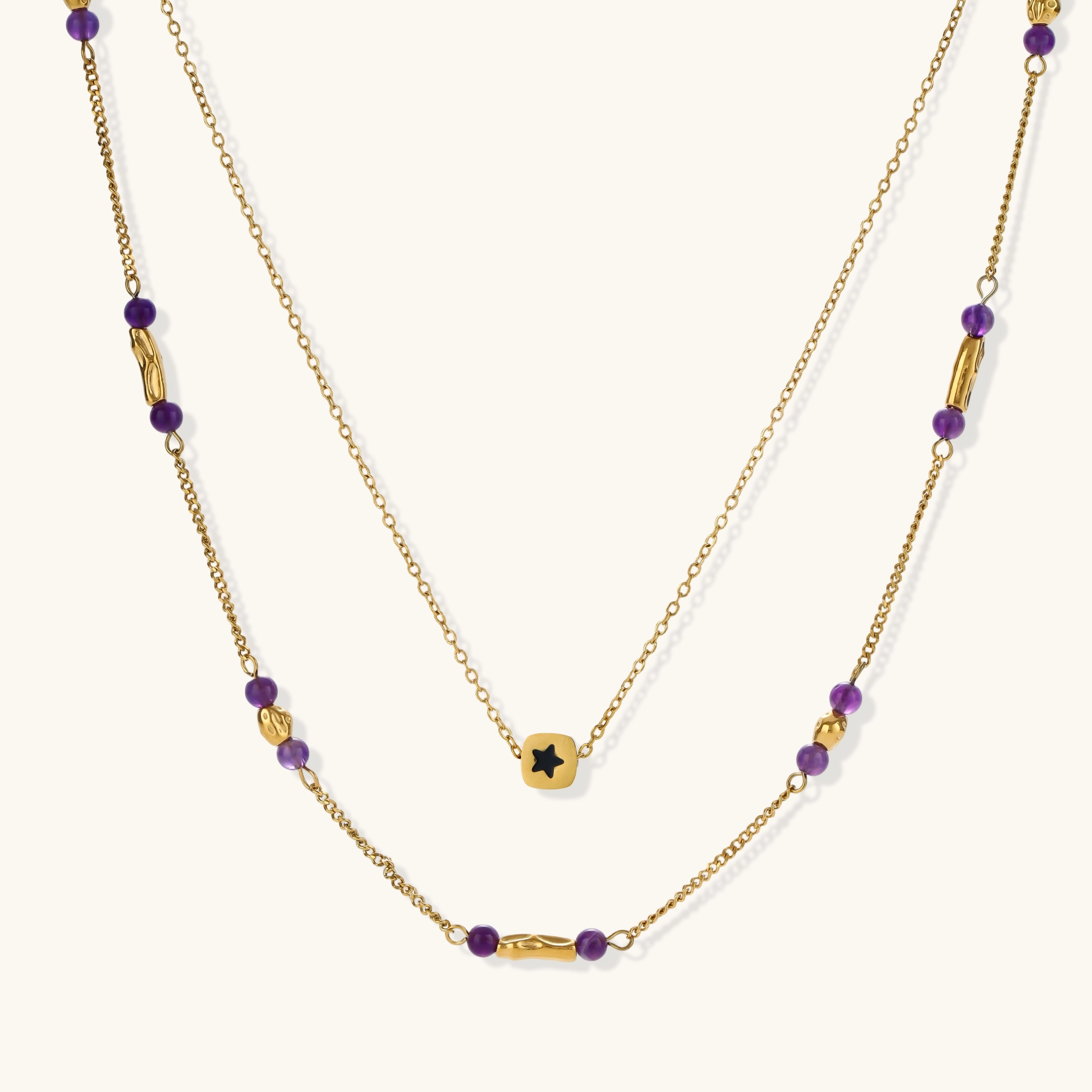 Two layered gold-tone necklaces with purple stone beads and star pendant against cream background.