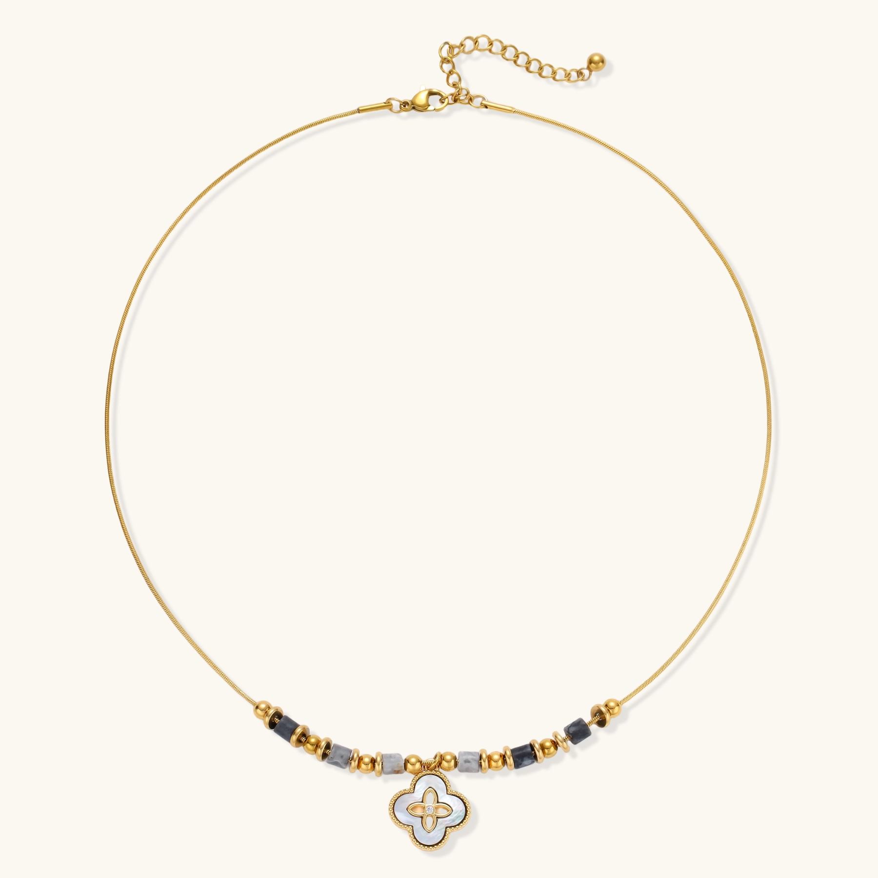 Gold-toned beaded necklace with grey stones and quatrefoil abalone shell pendant on cream background.