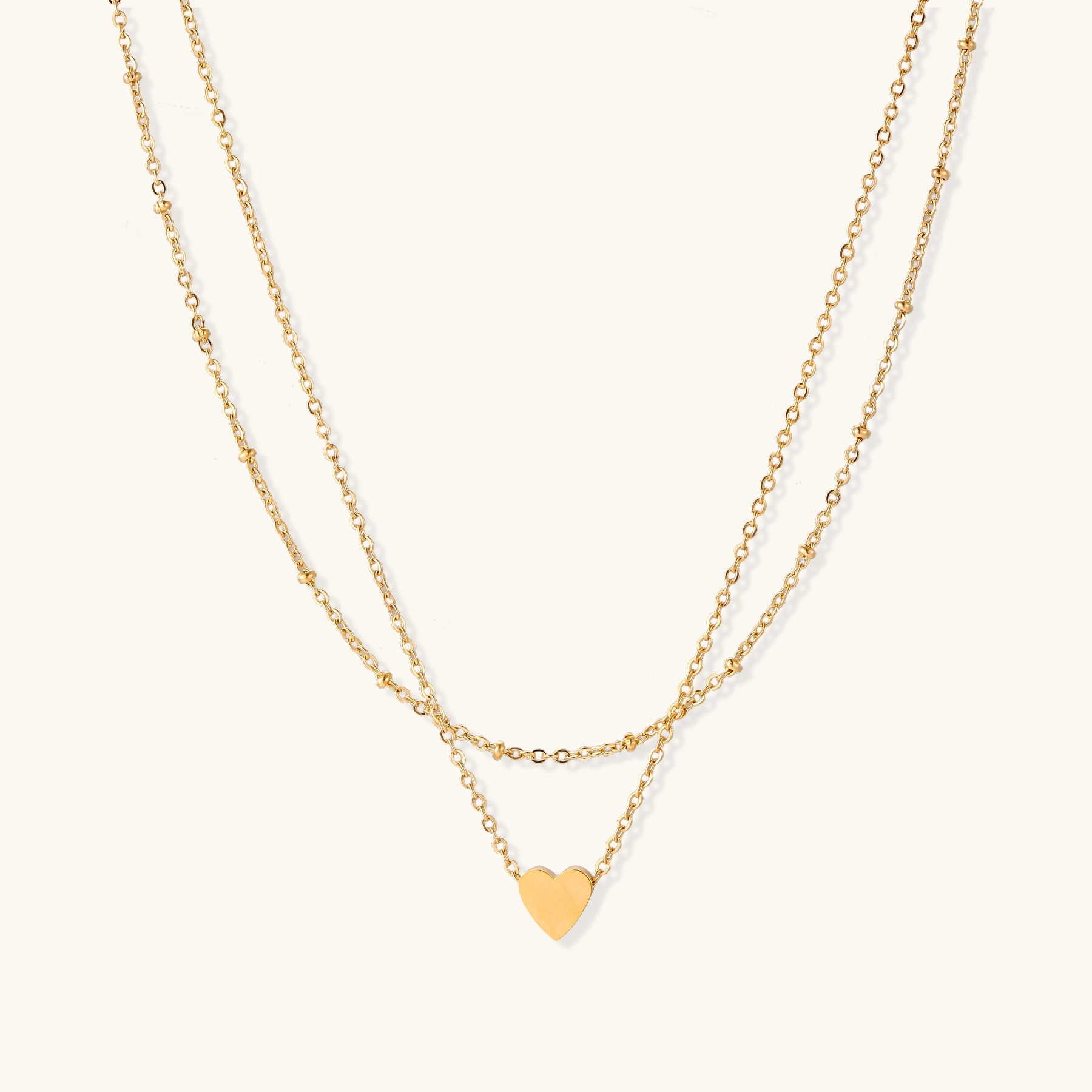 Delicate double-chain gold necklace with tiny heart pendant on cream background