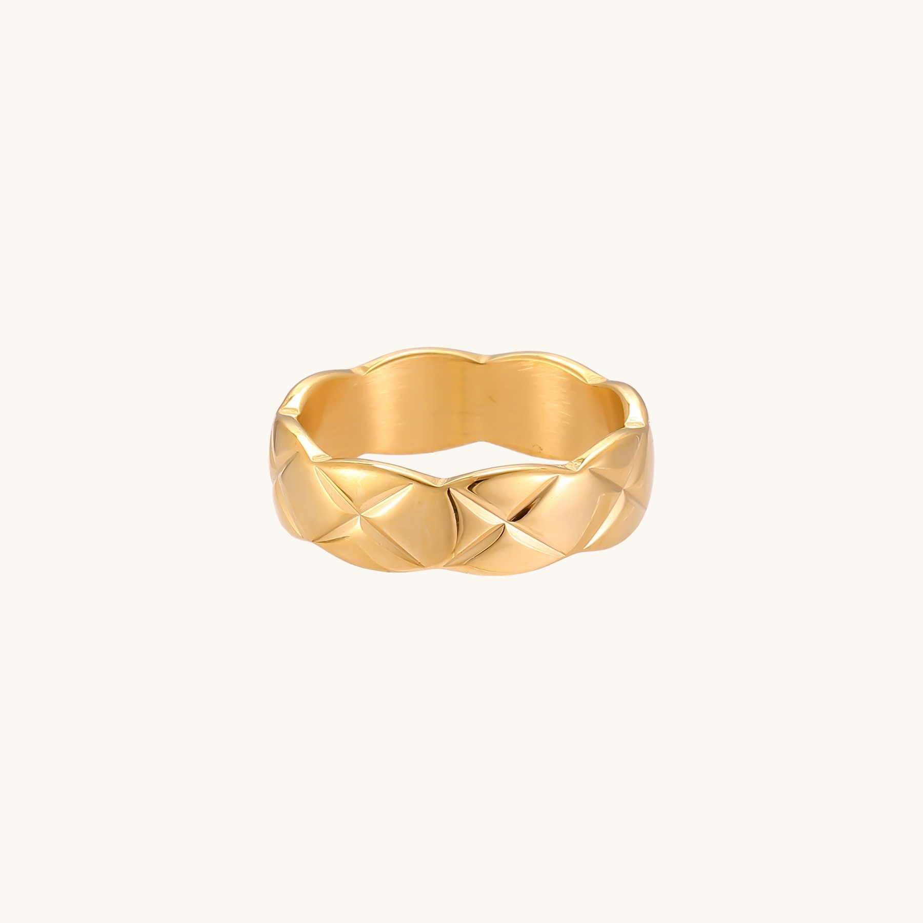 Close-up of an 18K gold-plated twisted band ring with dimensional braided pattern on cream background.