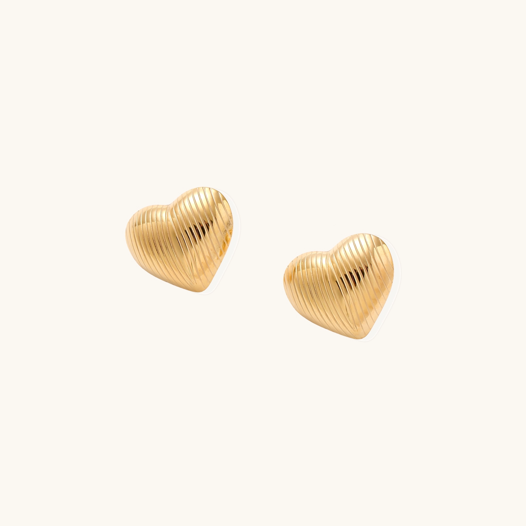 Gold heart-shaped stud earrings with parallel ridged texture on cream background