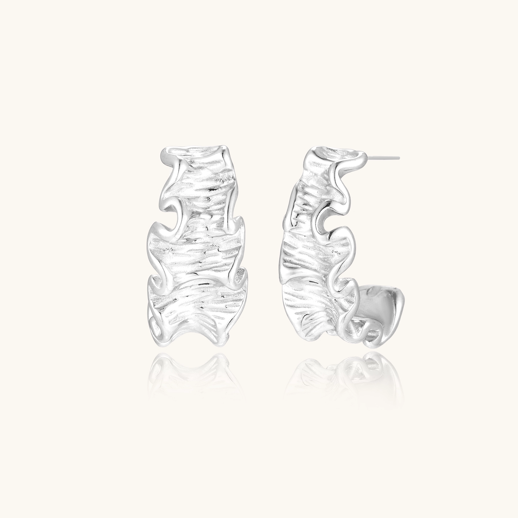 White gold plated sculptural hoop earrings with organic wavy edges and reflective metallic finish on cream background