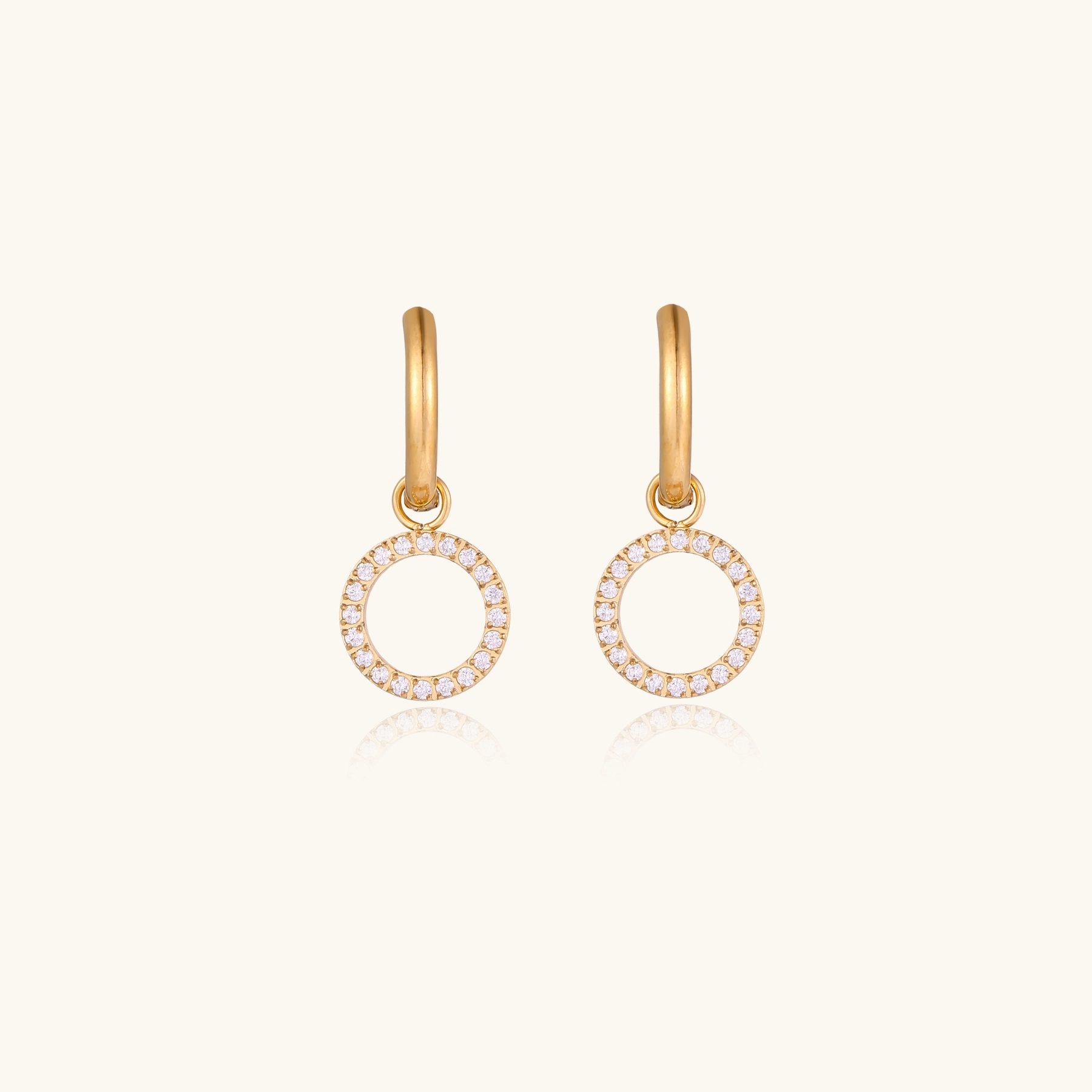Gold-plated huggie hoop earrings with CZ-studded open circle charms on beige background