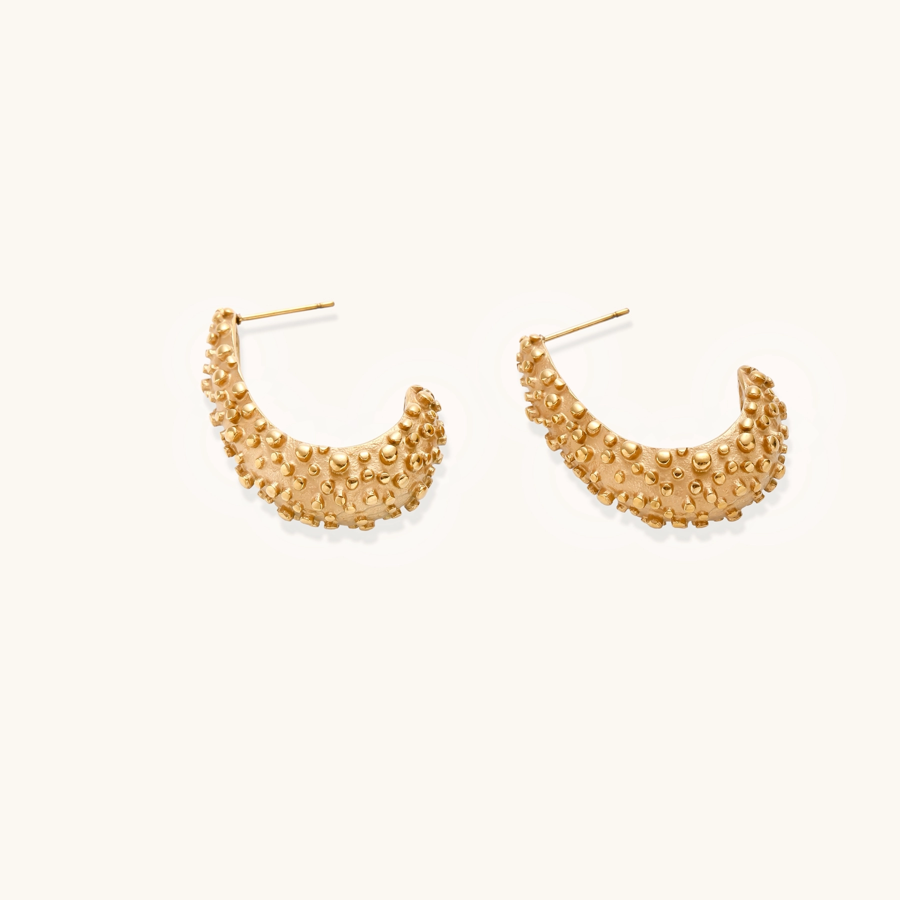 Curved gold hoop earrings with raised granulated texture resembling sea urchin surface on cream background