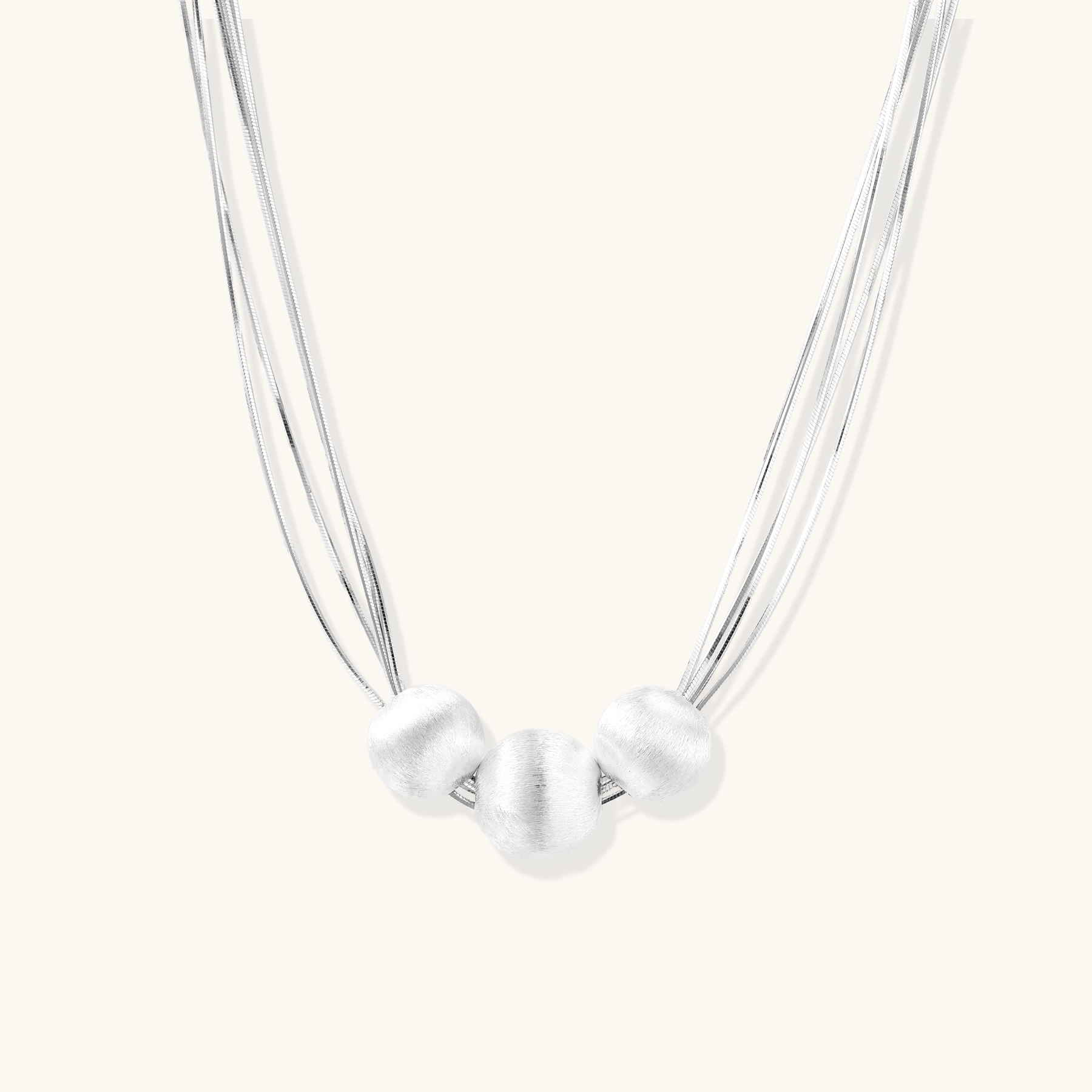 Sterling silver multi-strand necklace with three brushed round beads on cream background