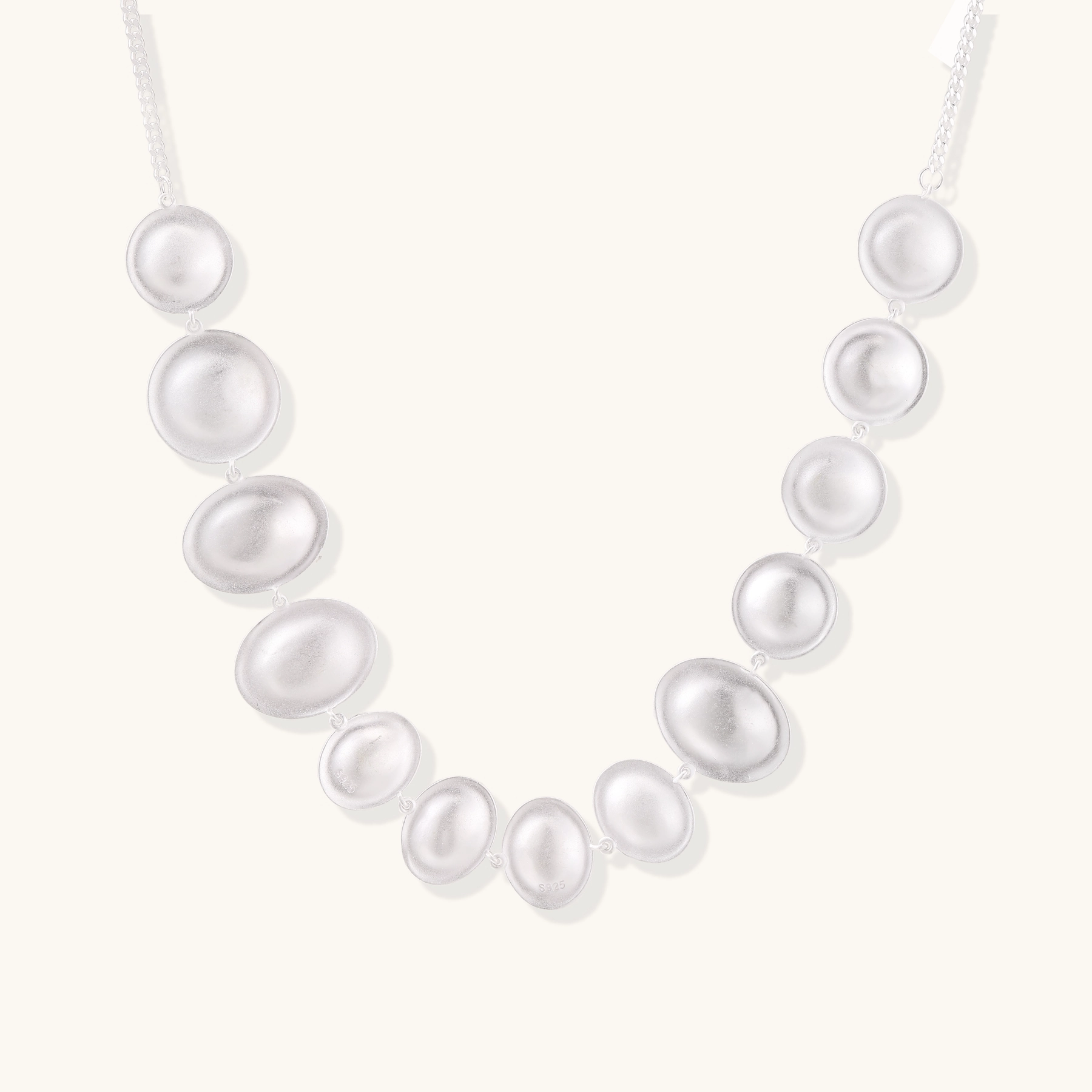 Graduated pearl-finish silver discs forming an organic bubble bib necklace on delicate chain against cream background.