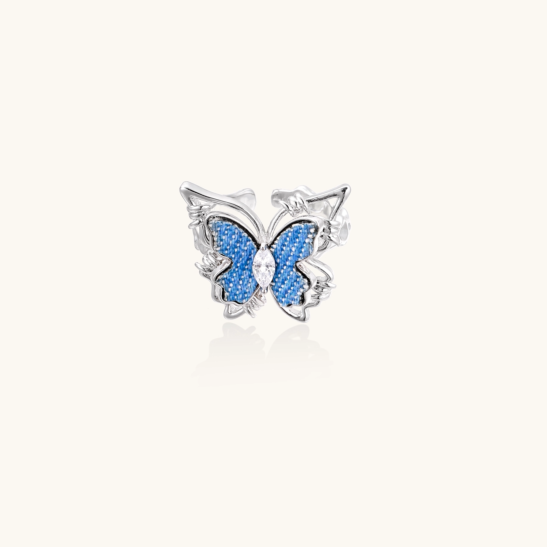 Silver-toned ring with blue denim butterfly wings, marquise zirconia center, and ornate scrollwork band on white background