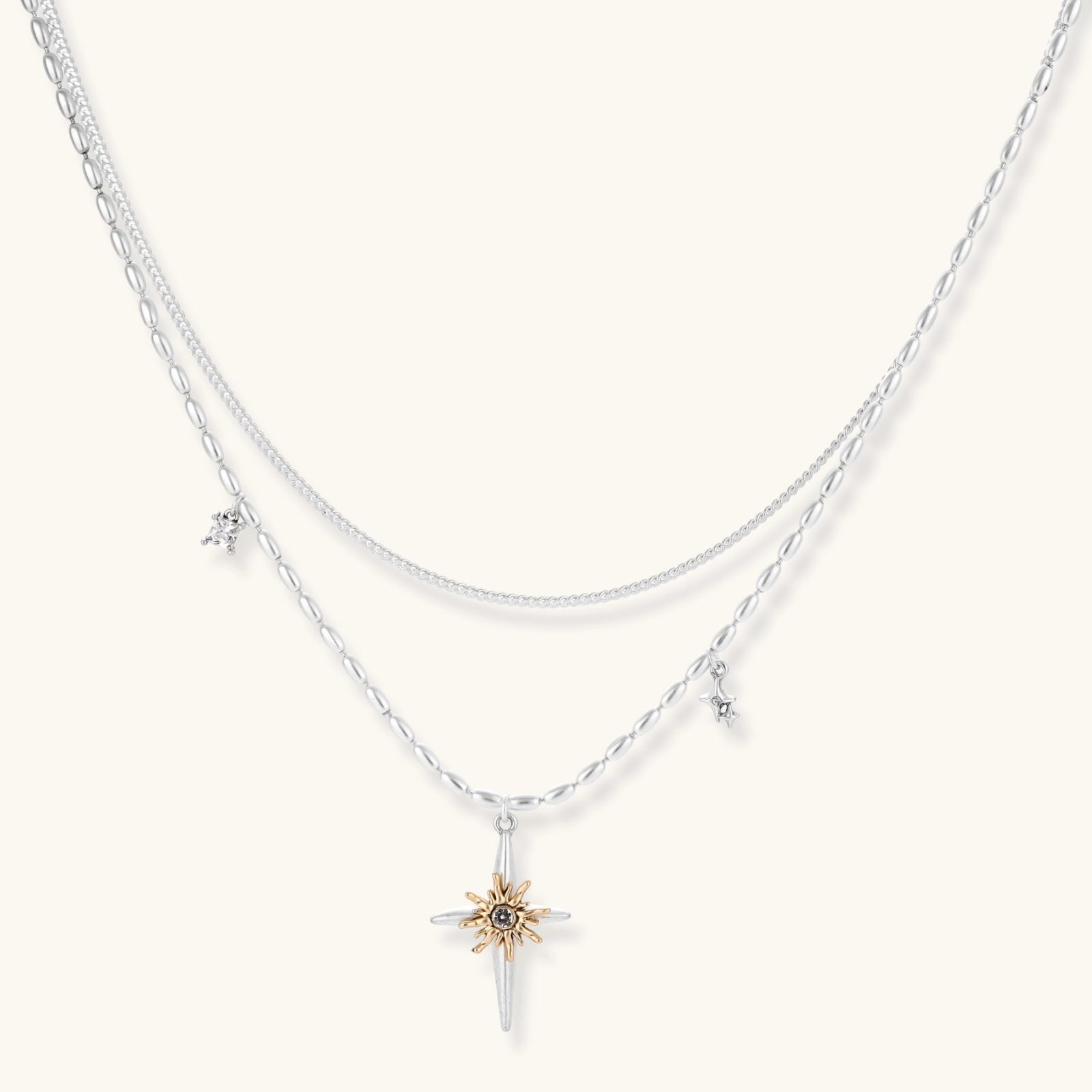 Two-layer silver-toned necklace with star charms and dagger pendant featuring golden sun motif on white background.
