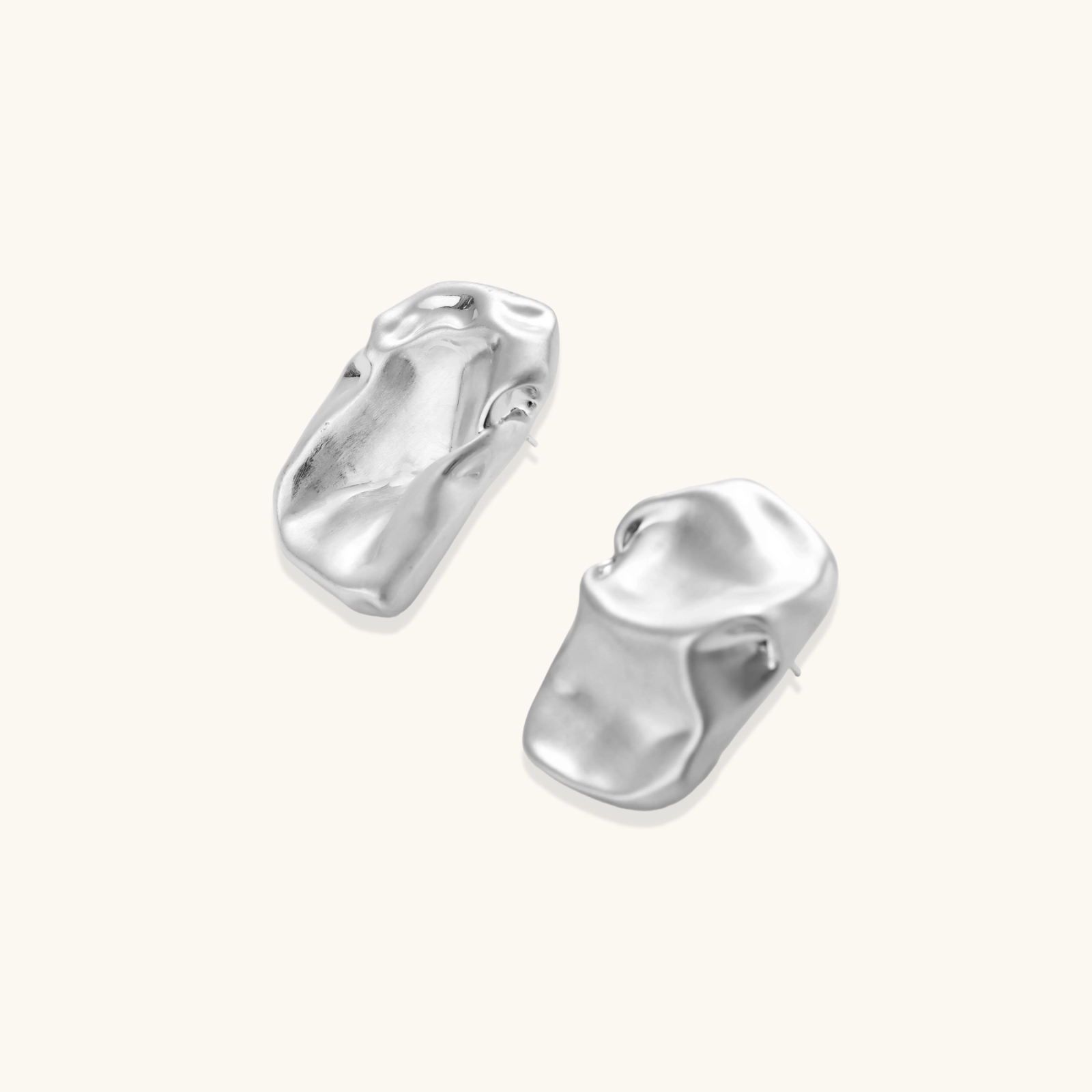 Abstract crumpled metallic earrings with fluid organic shapes in reflective gold and silver finish on neutral background.