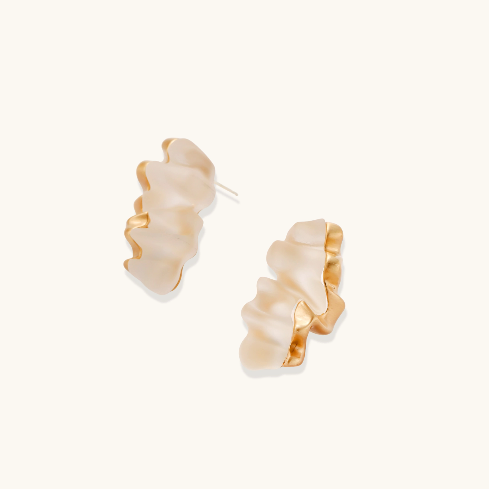Sculptural wave-textured statement earrings with flowing organic ridges in metallic finish on cream background