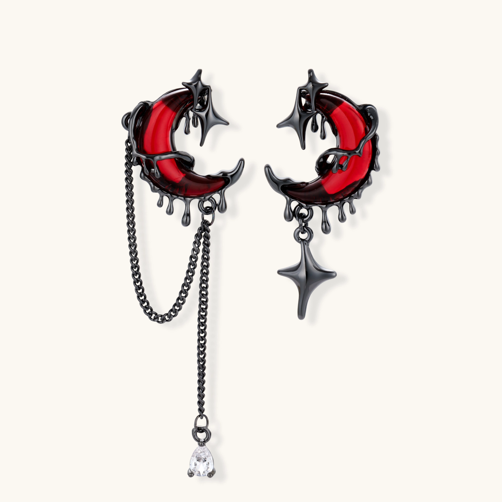 Gothic asymmetrical earrings with red crescent moons, black dripping stars, chains and crystal drop on white background.