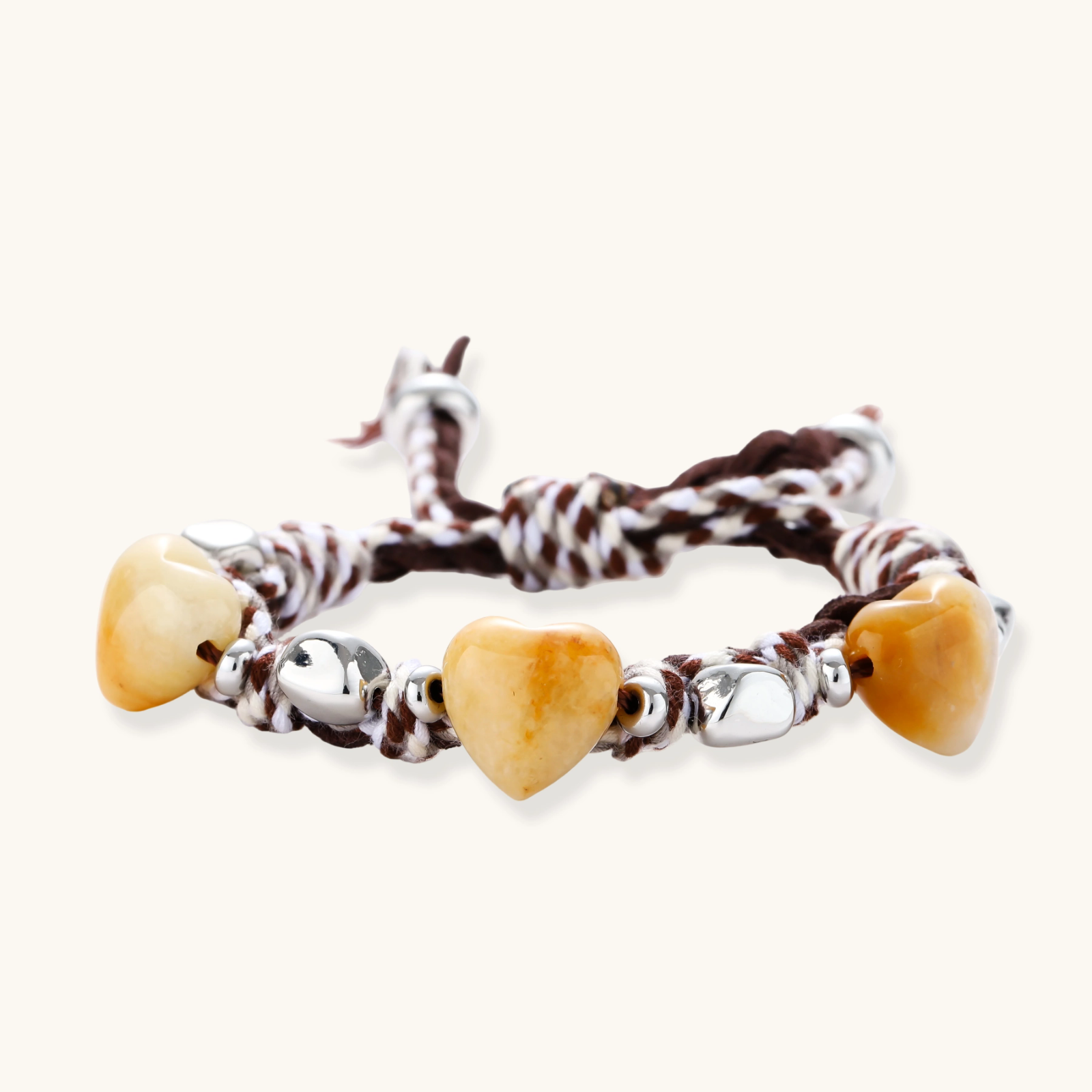 Braided brown and cream suede cord bracelet with heart-shaped amber gemstones and brass beads on white background.