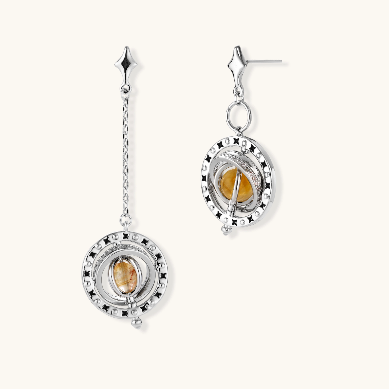 Asymmetrical stud earrings with concentric rings and amber zirconia stones, one with chain drop, in silver finish