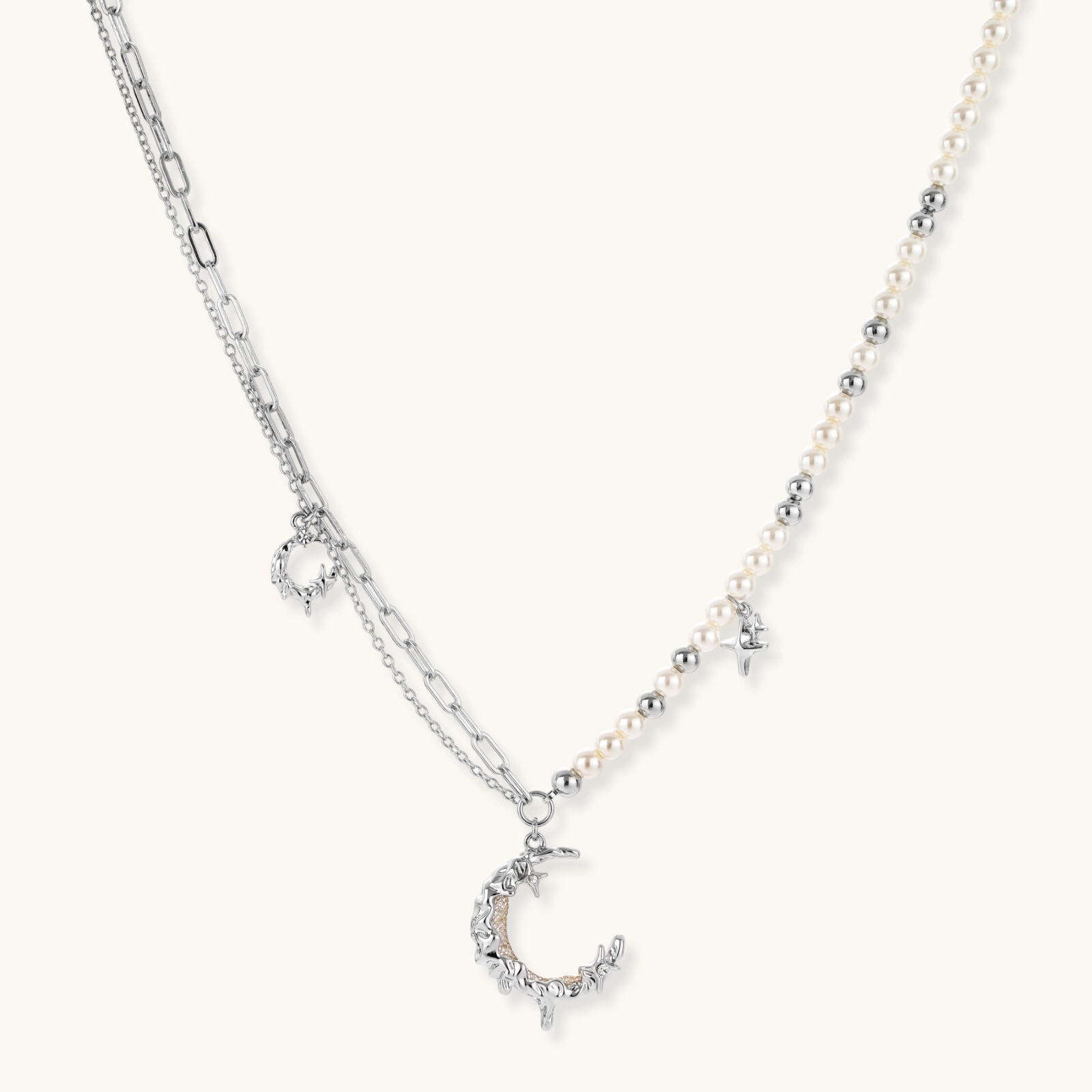 Silver-toned crescent moon pendant with star accents on pearl and chain necklace against white background.