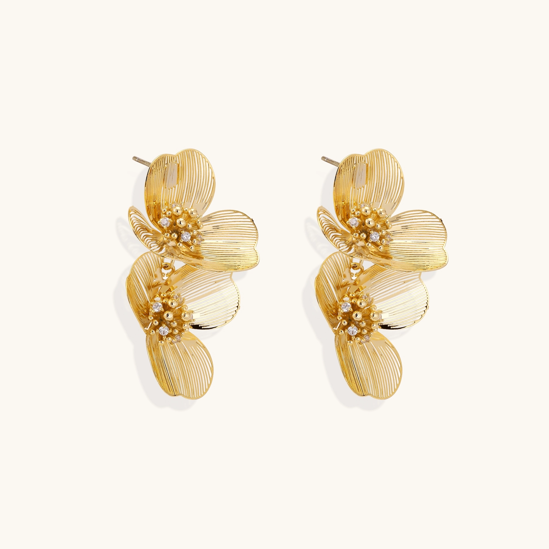 Pair of gold-plated double flower earrings with textured petals and crystal centers on cream background.