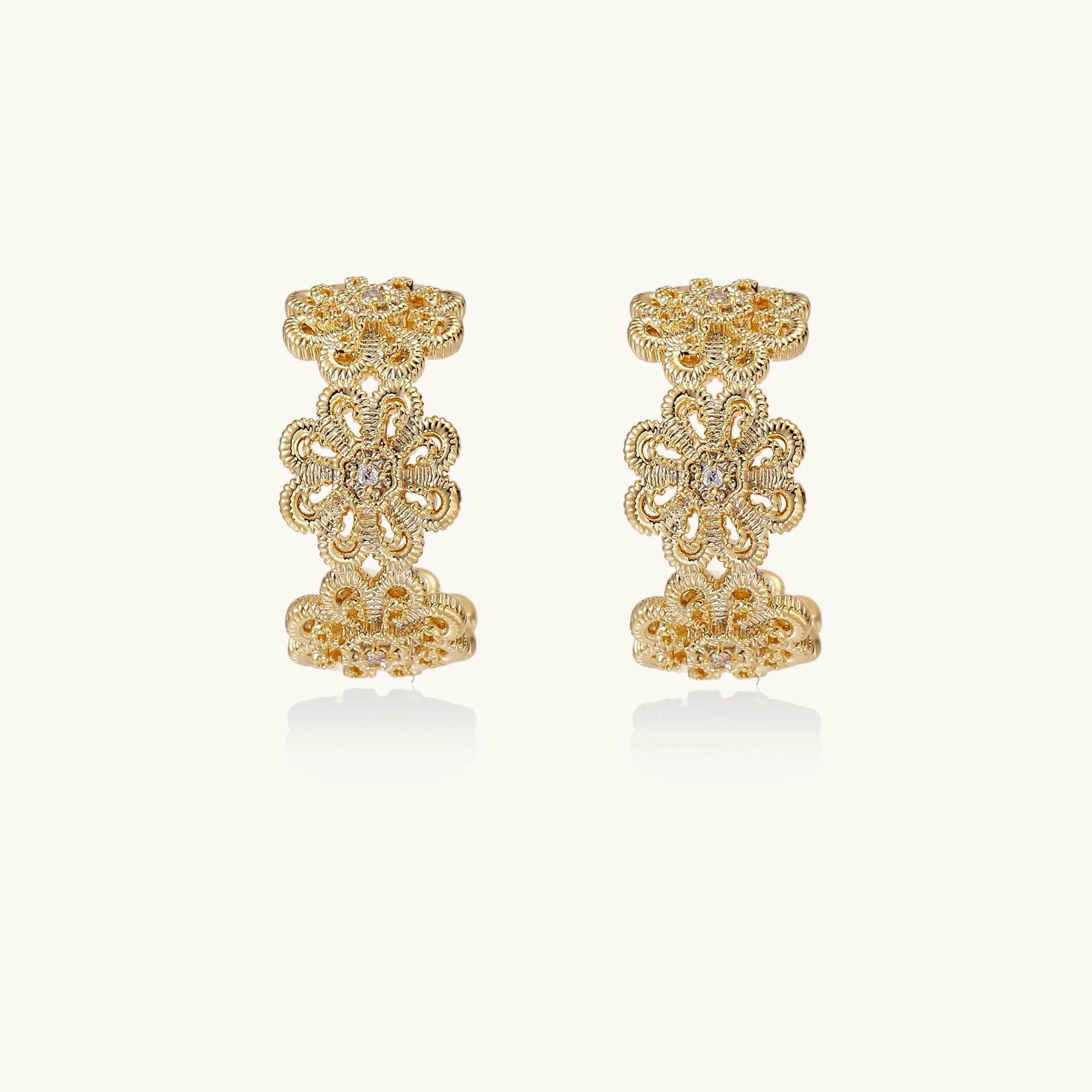 Gold hoop earrings with intricate three-dimensional floral filigree pattern in 14K gold plated brass on cream background