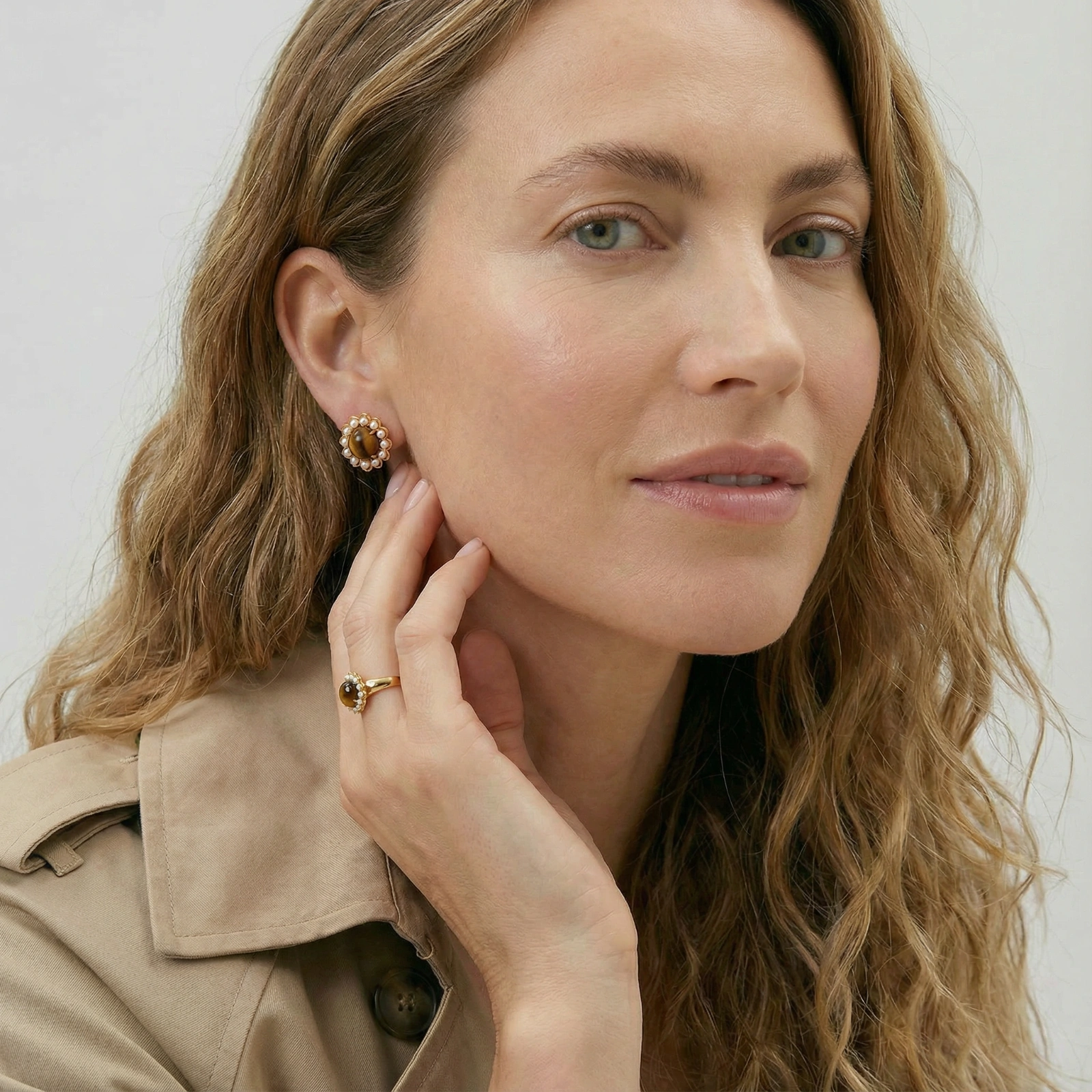 Gold-plated stud earrings with cushion-cut tiger's eye stones surrounded by pearl halos on white background.