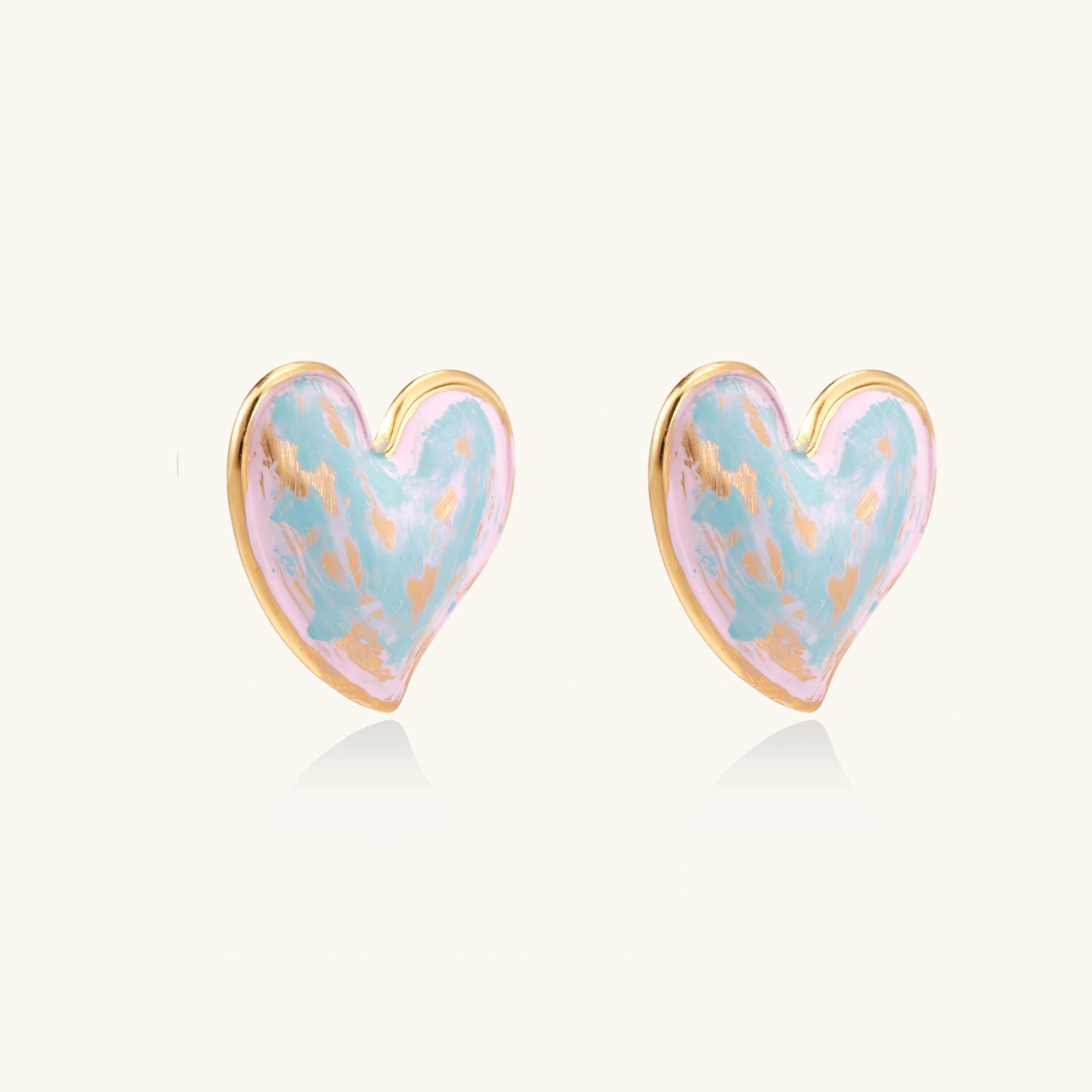 Heart-shaped stud earrings with swirled turquoise and pink enamel in gold-plated frames on cream background
