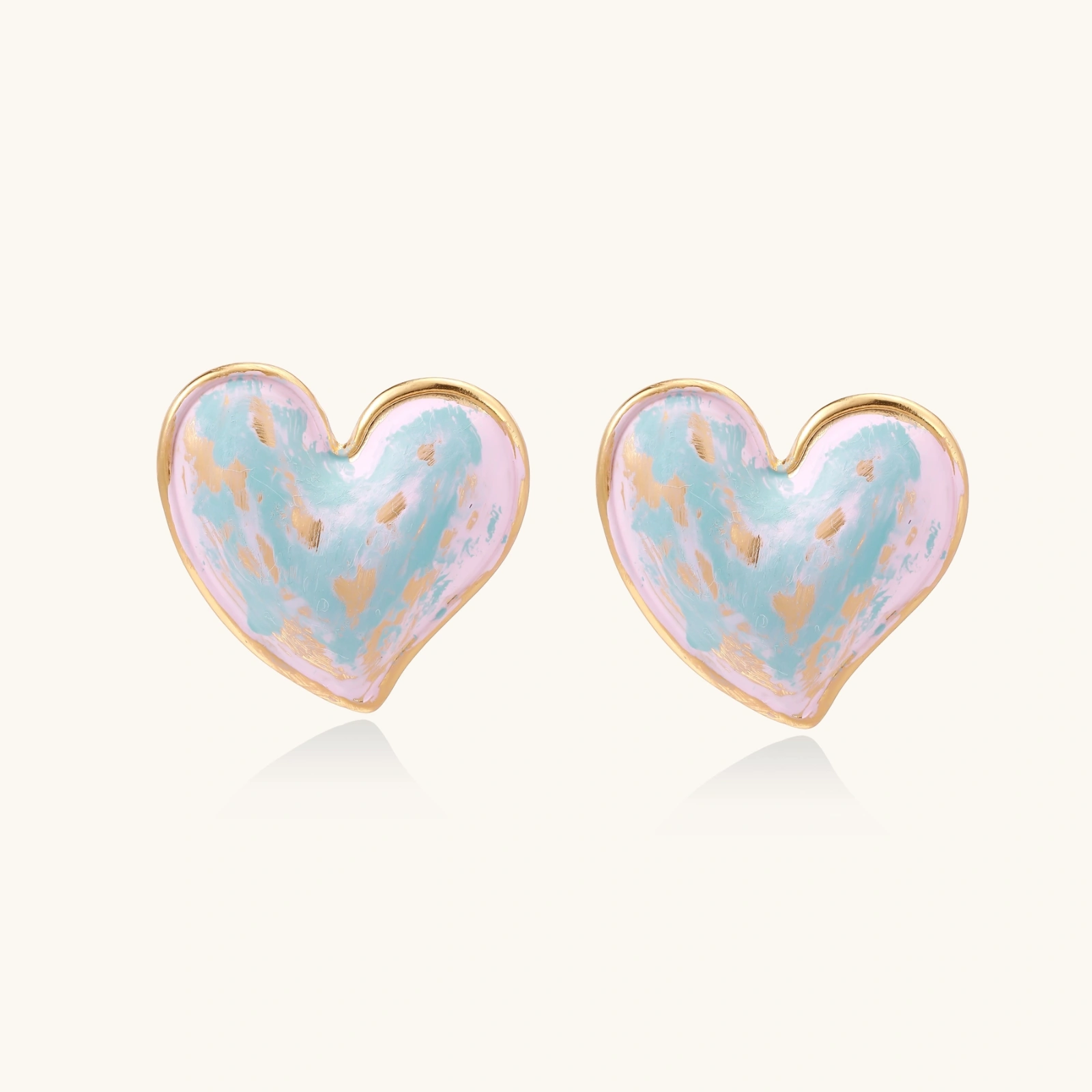 Heart-shaped stud earrings with swirled turquoise and pink enamel in gold-plated frames on cream background