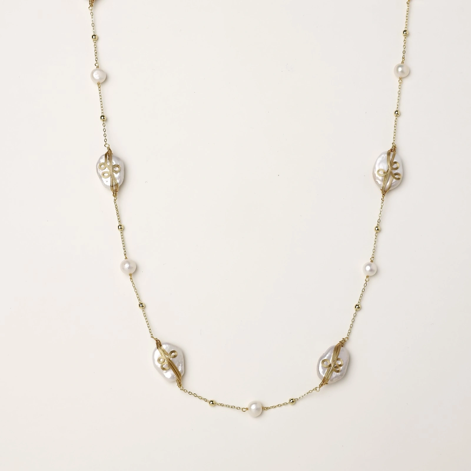 Long gold chain necklace with baroque pearls wrapped in leaf designs and small freshwater pearls spaced along the strand
