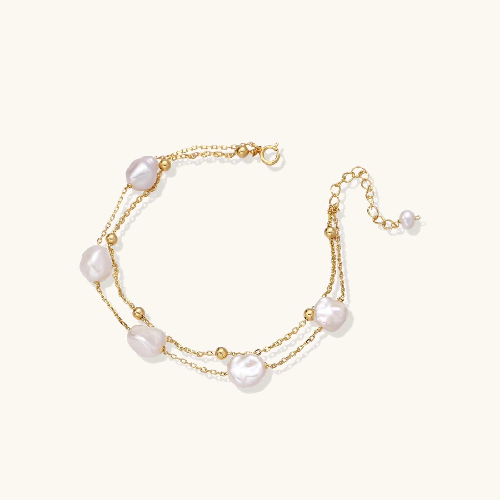 Double-strand gold bracelet with irregular baroque pearls and smooth freshwater pearls on cream background.