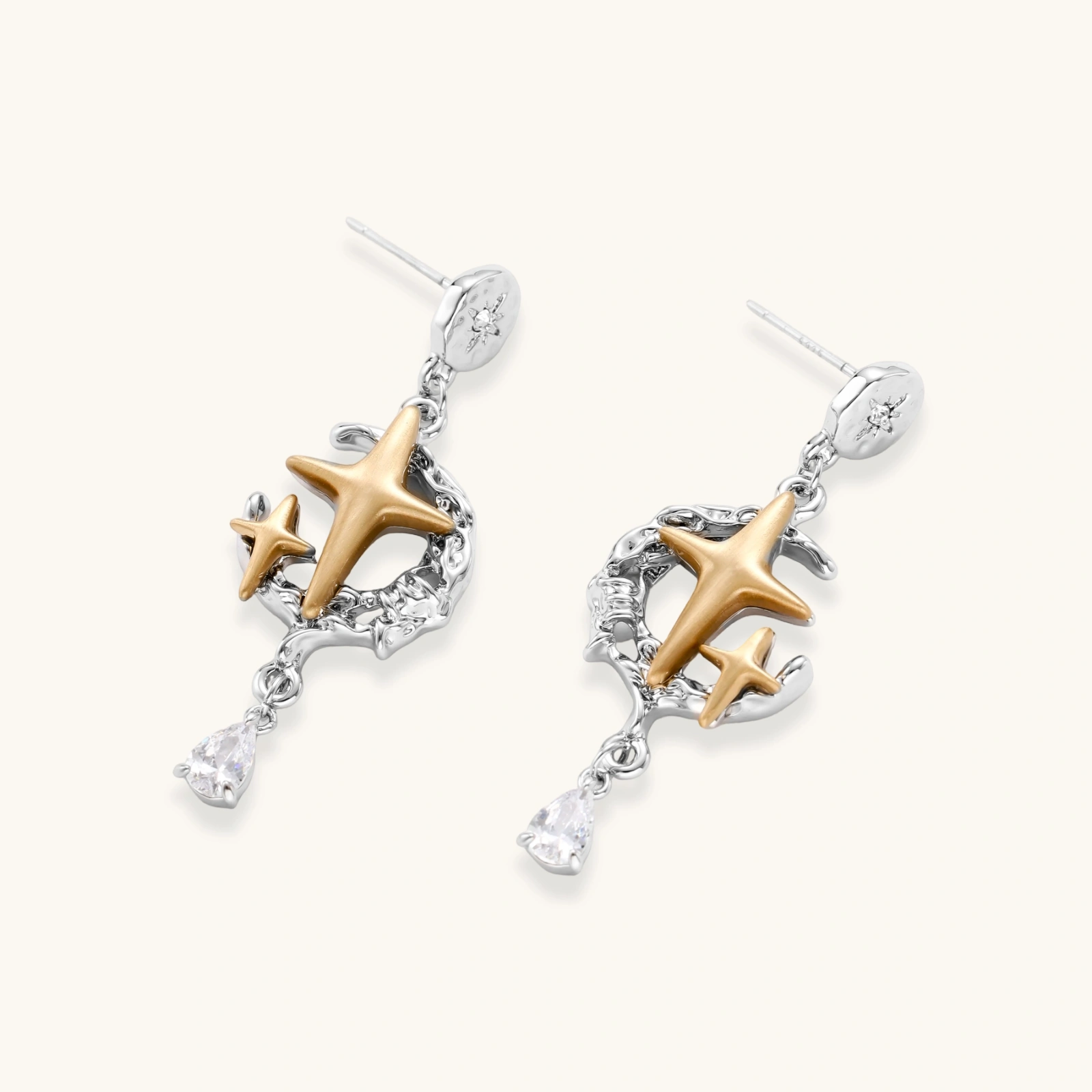 Two-tone star earrings with gold celestial motifs, silver chains, and clear crystal droplets on white background.
