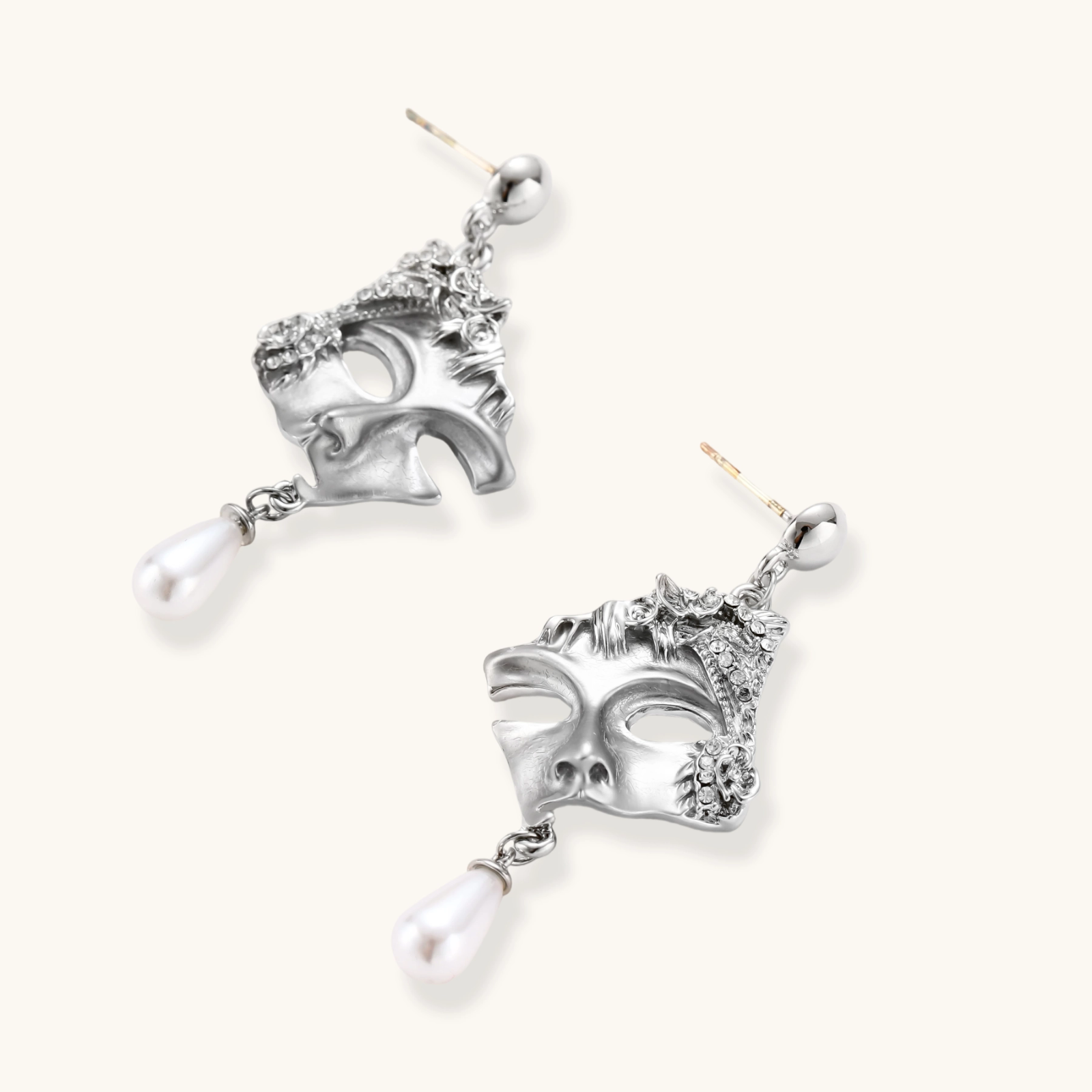 Ornate silver-toned theatrical mask earrings with crystal details and pearl drops on white background.