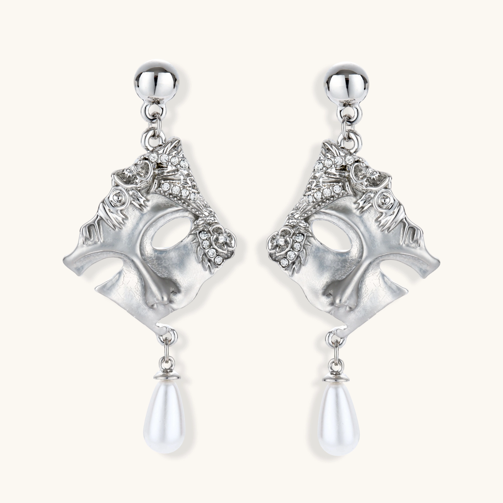 Ornate silver-toned theatrical mask earrings with crystal details and pearl drops on white background.