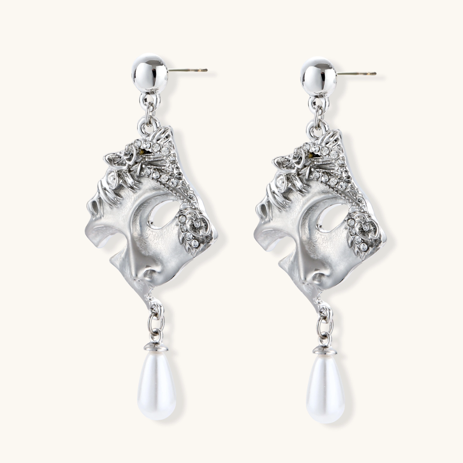 Ornate silver-toned theatrical mask earrings with crystal details and pearl drops on white background.