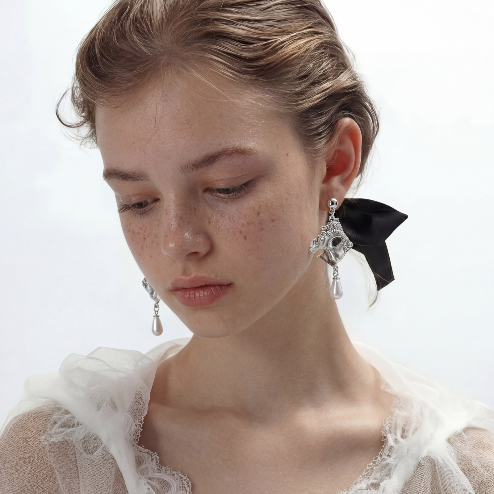 Ornate silver-toned theatrical mask earrings with crystal details and pearl drops on white background.