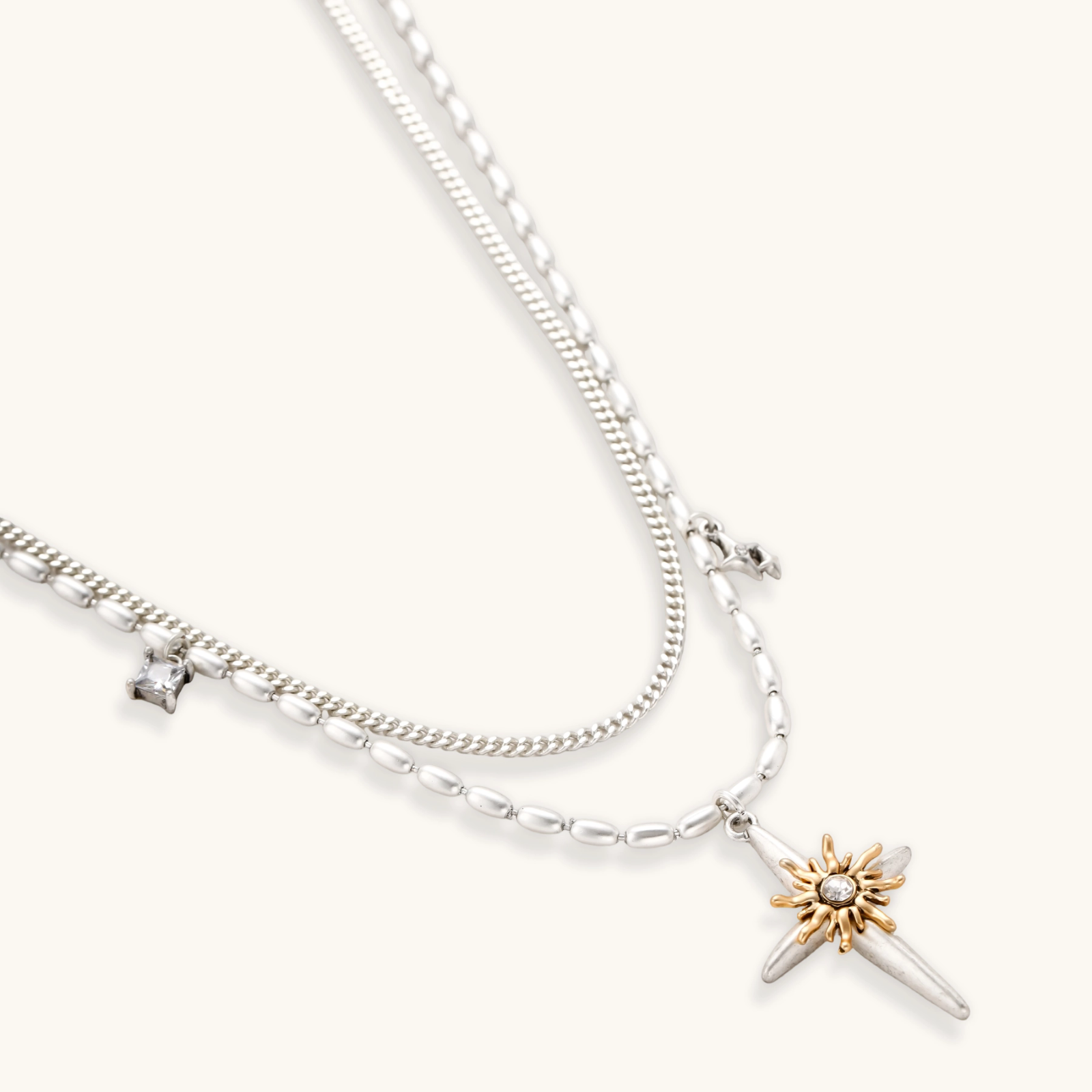 Two-layer silver-toned necklace with star charms and dagger pendant featuring golden sun motif on white background.