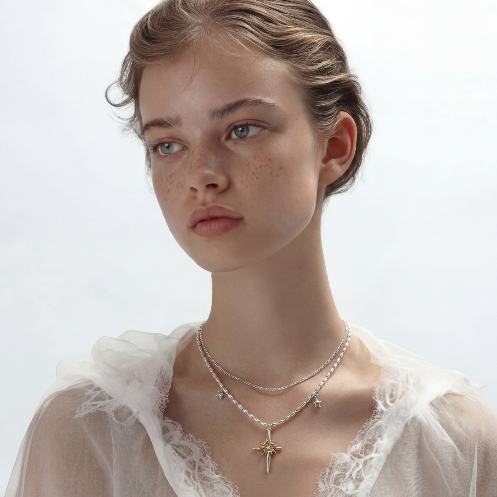 Two-layer silver-toned necklace with star charms and dagger pendant featuring golden sun motif on white background.