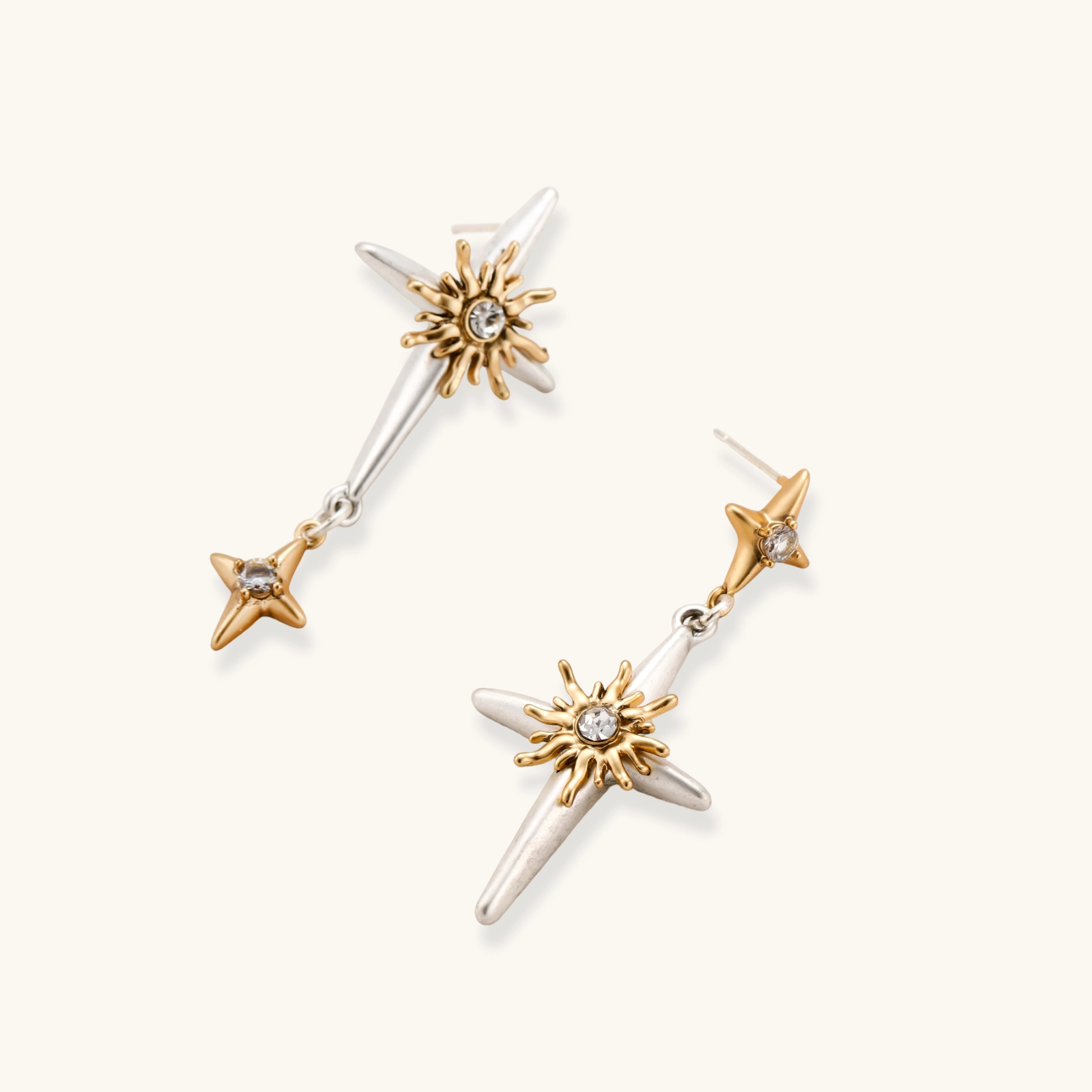 Dangle earrings with silver hoops, gold sun charms with crystals, and gold four-pointed star drops on cream background.