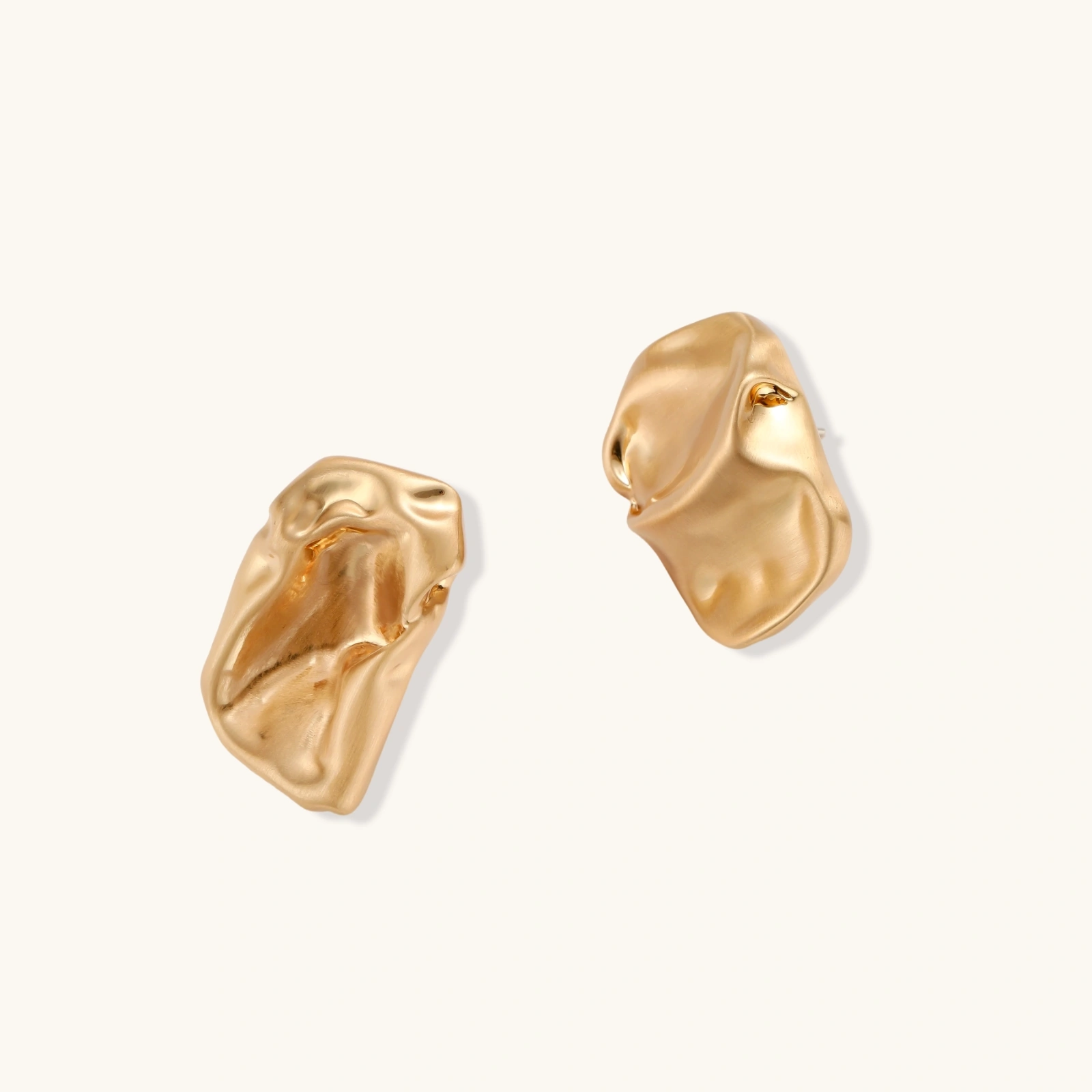 Abstract crumpled metallic earrings with fluid organic shapes in reflective gold and silver finish on neutral background.