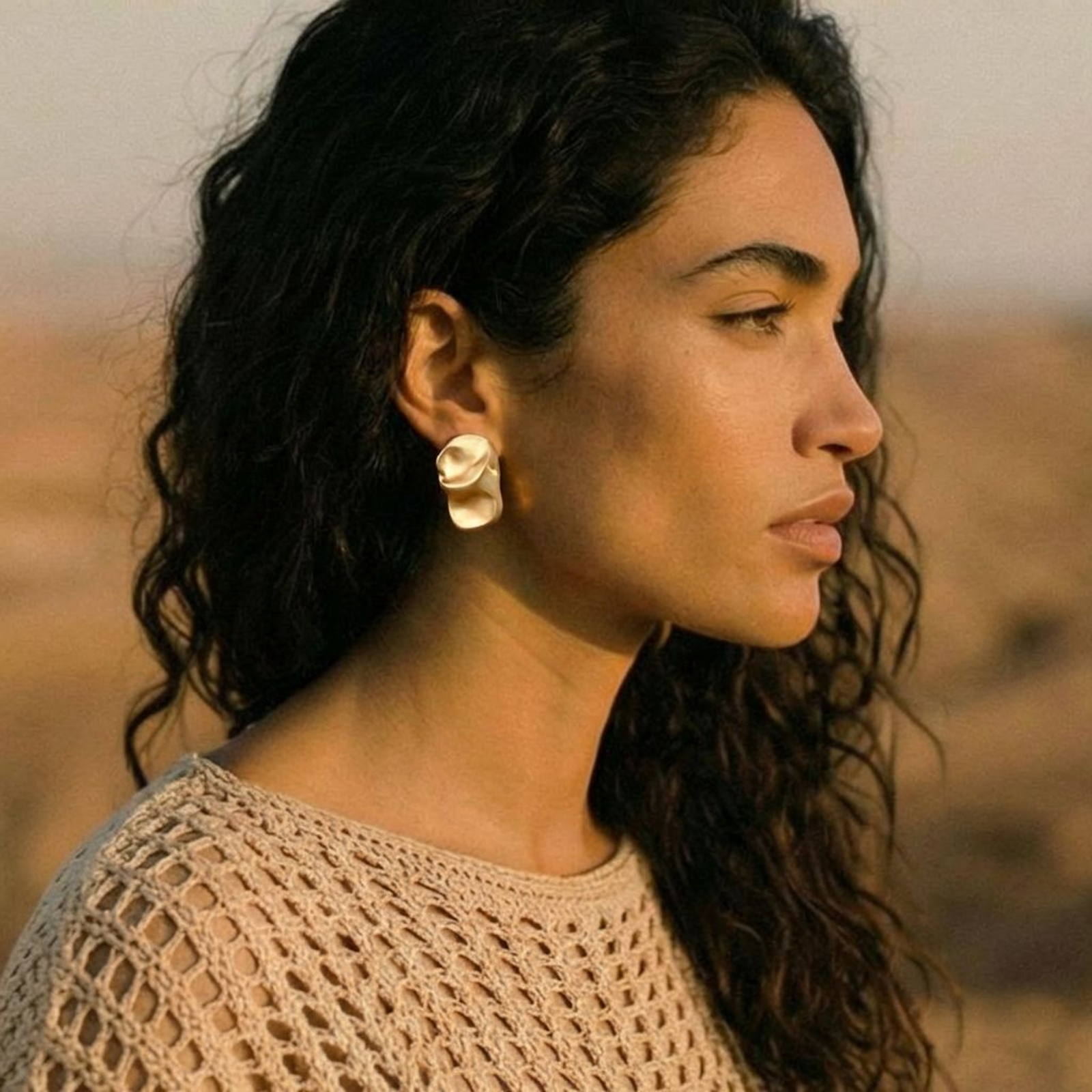 Abstract crumpled metallic earrings with fluid organic shapes in reflective gold and silver finish on neutral background.