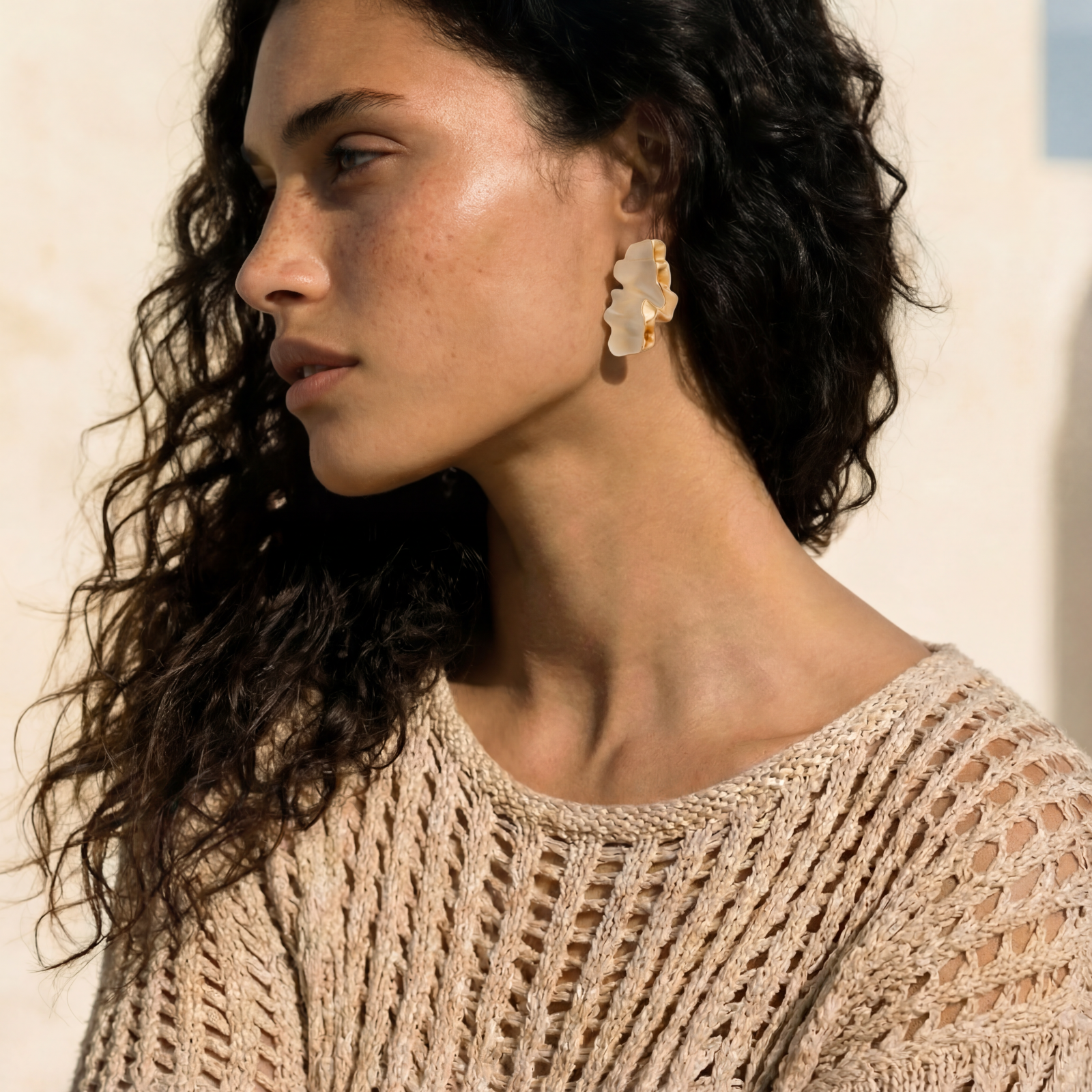 Sculptural wave-textured statement earrings with flowing organic ridges in metallic finish on cream background