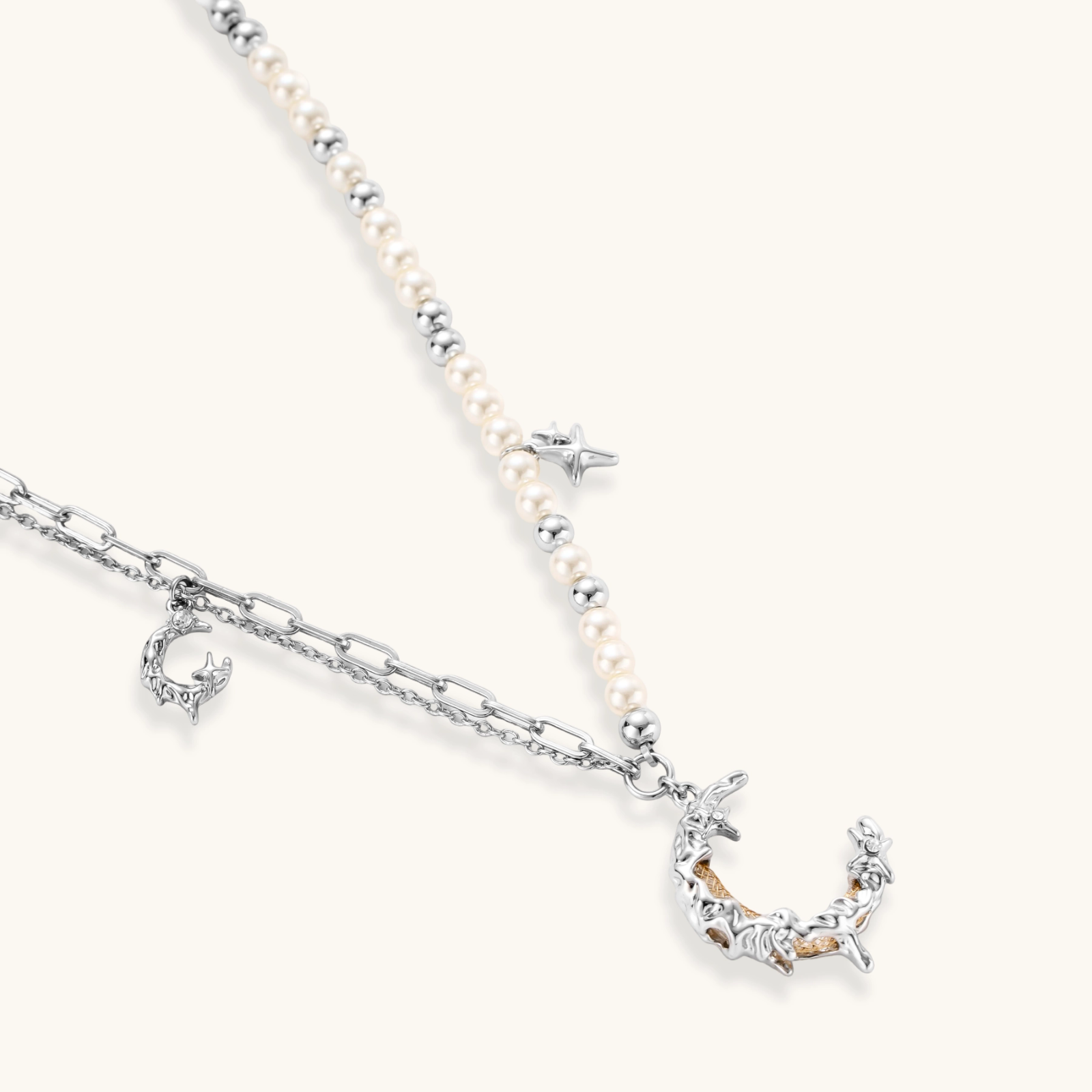 Silver-toned crescent moon pendant with star accents on pearl and chain necklace against white background.