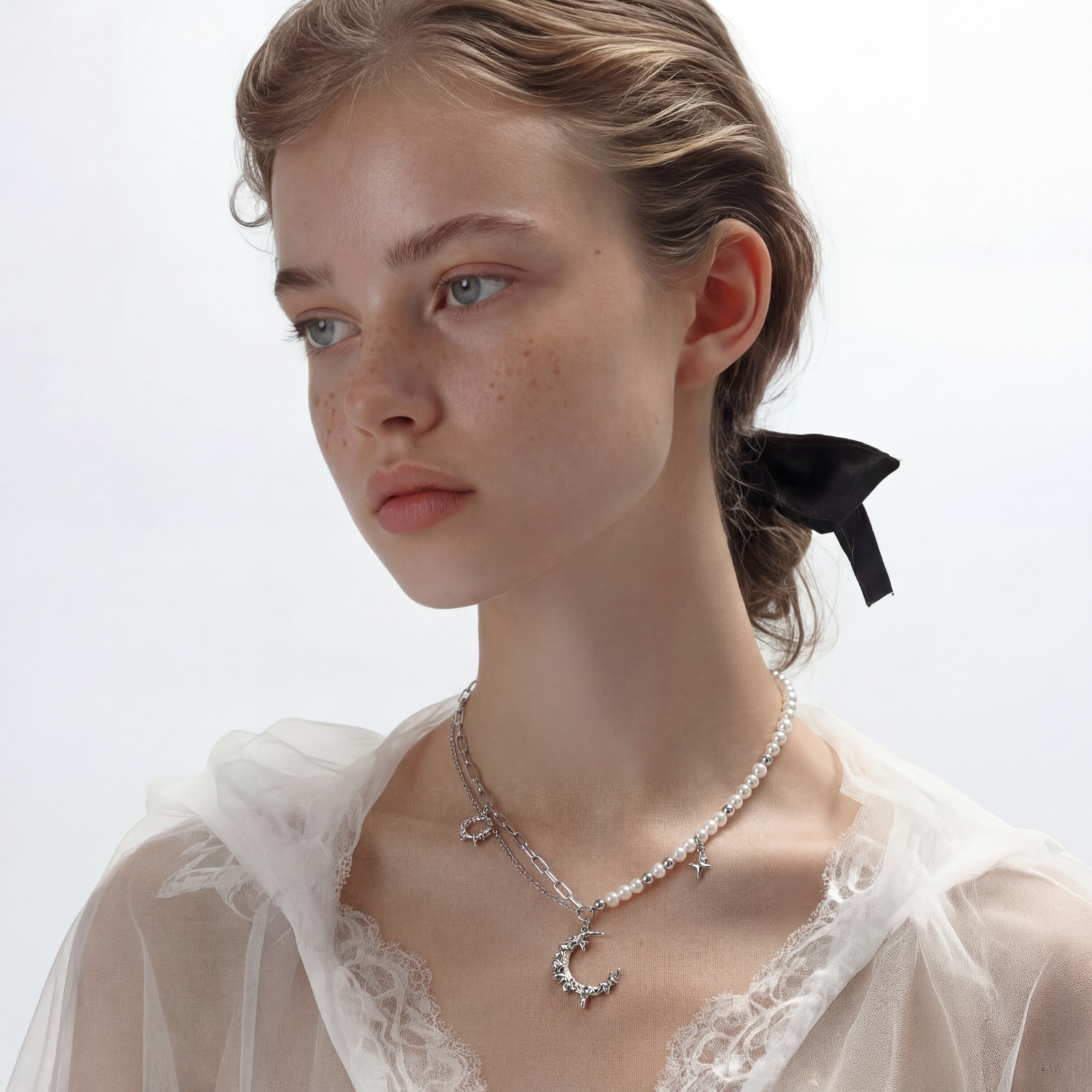 Silver-toned crescent moon pendant with star accents on pearl and chain necklace against white background.