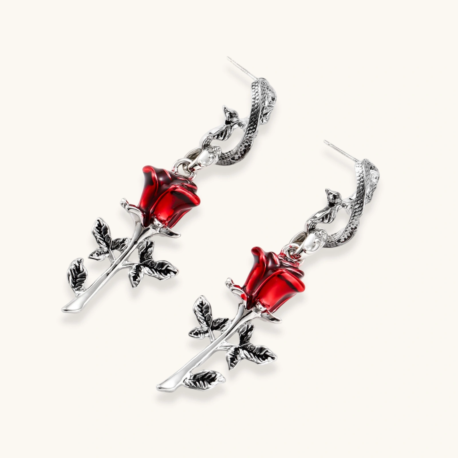Gothic dangle earrings featuring silver serpent hooks with red enamel roses and metallic stems on white background.