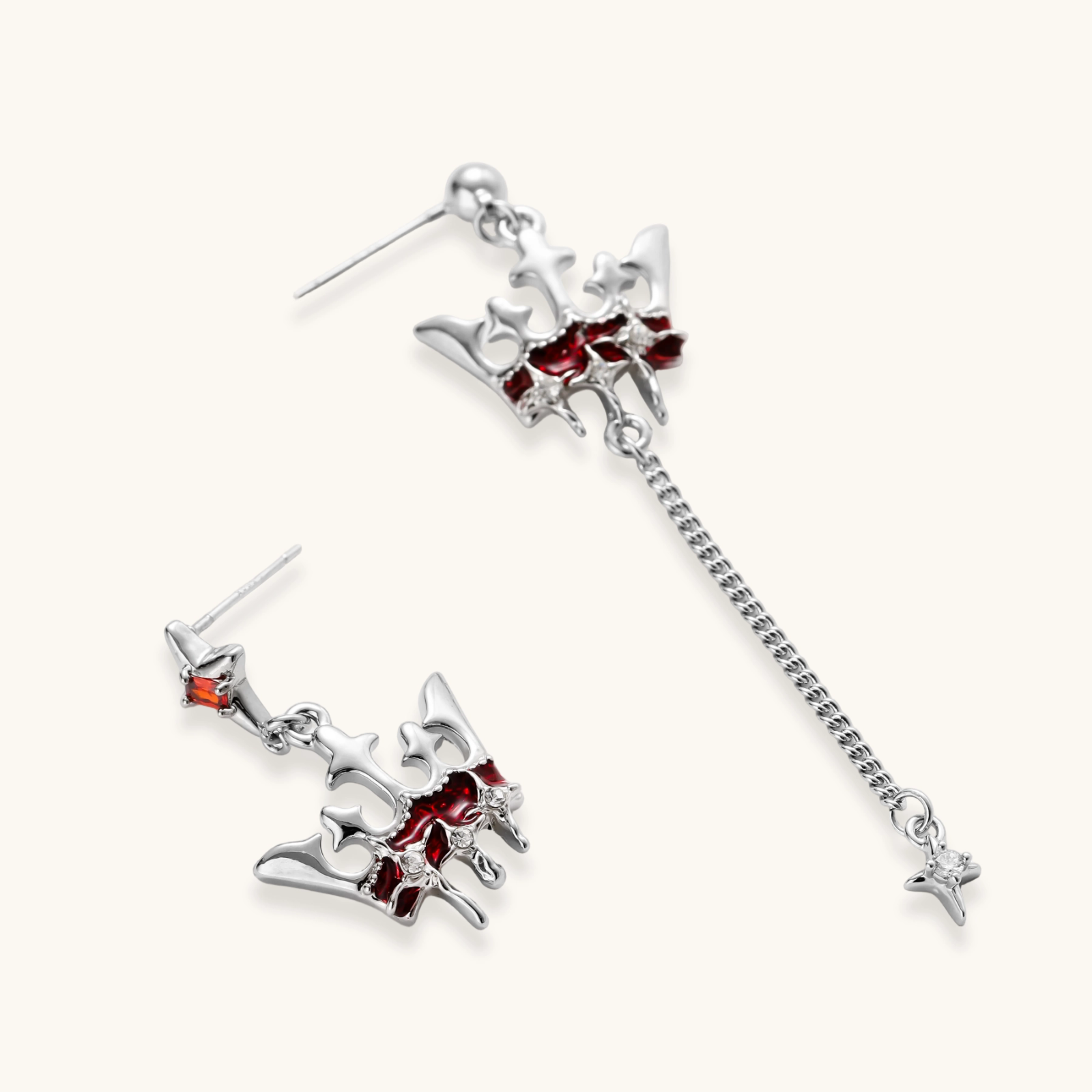 Asymmetrical crown-shaped stud earrings with red zirconia stones, one featuring a silver chain with star charm