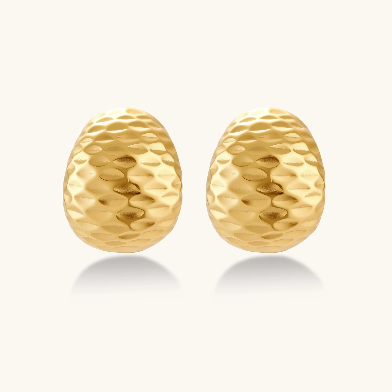 Pair of textured gold-plated sterling silver huggie earrings with dimpled surface finish on cream background.