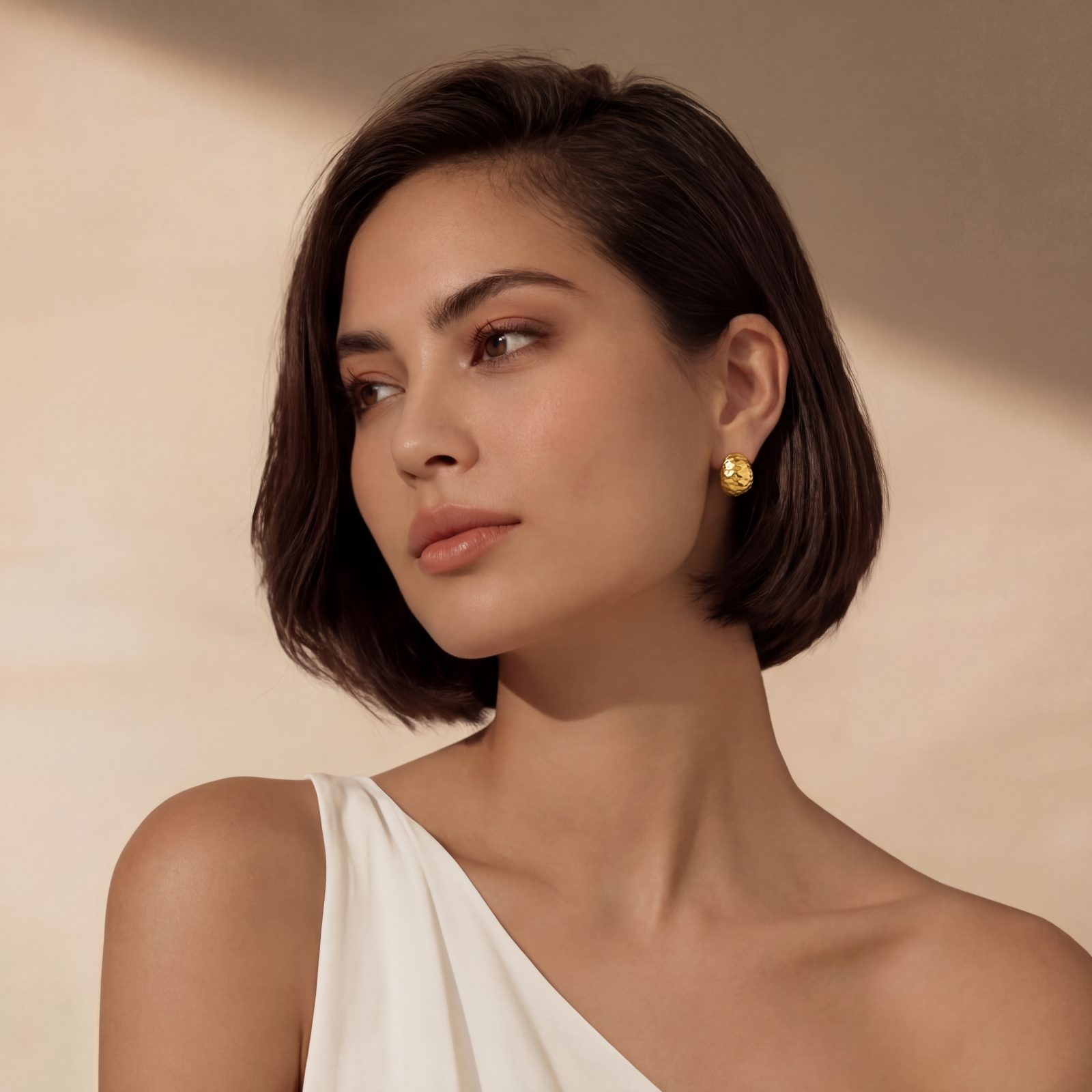 Pair of textured gold-plated sterling silver huggie earrings with dimpled surface finish on cream background.