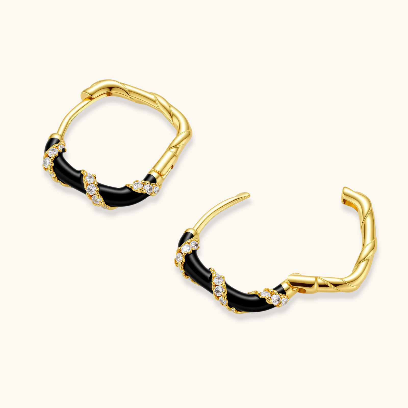 Small gold-plated hoop earrings with black enamel stripes and cubic zirconia crystals on white background.