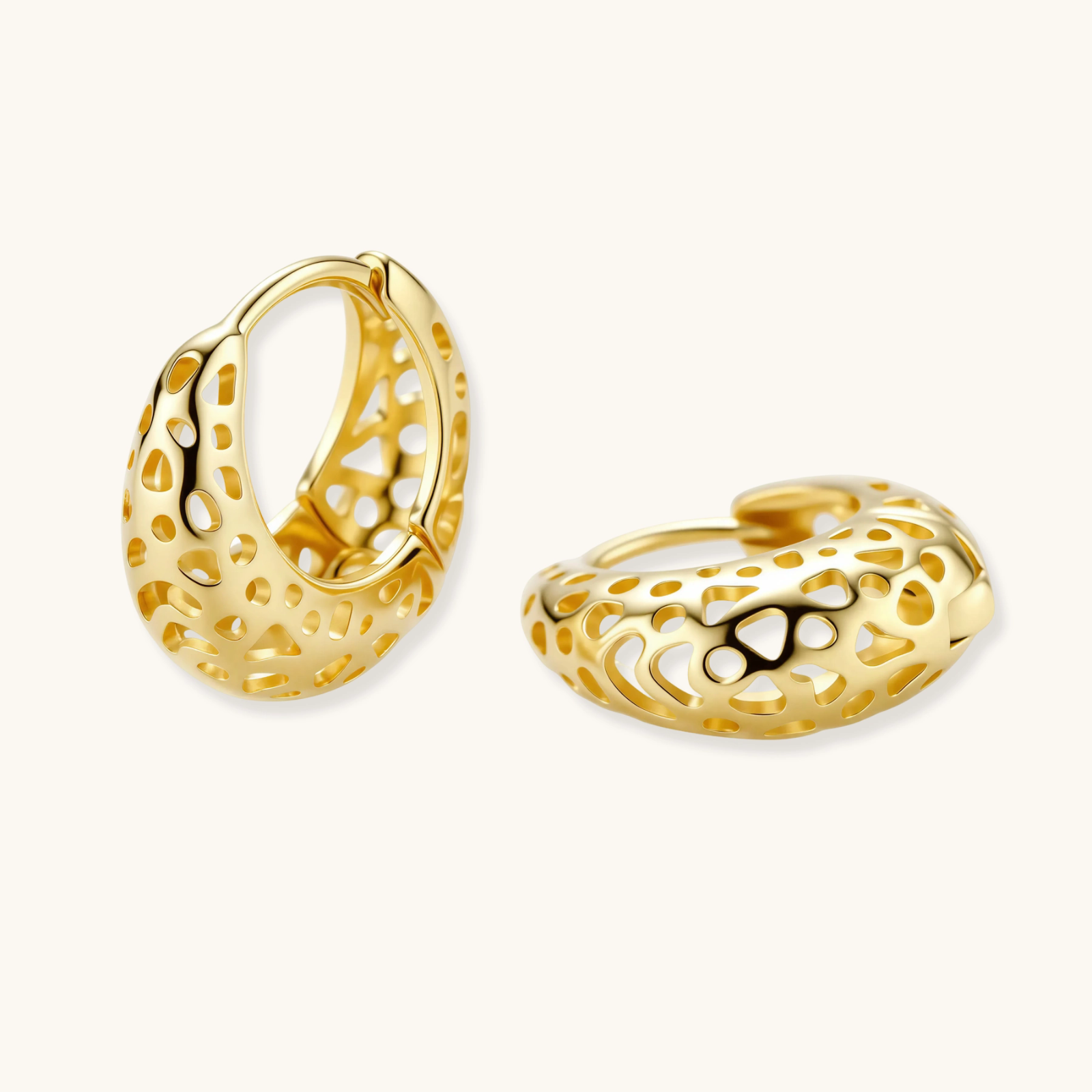 Close-up of small gold-plated hoop earrings with intricate honeycomb cutout pattern on cream background.