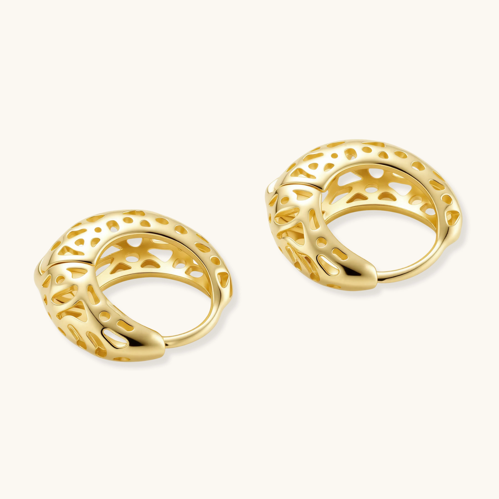 Close-up of small gold-plated hoop earrings with intricate honeycomb cutout pattern on cream background.