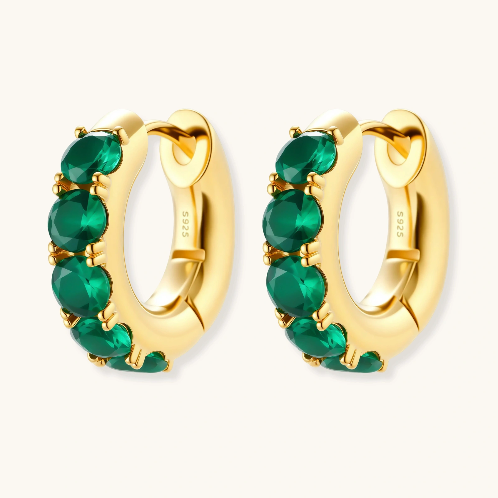 Close-up of gold-plated huggie hoop earrings featuring four emerald green cubic zirconia stones on white background.